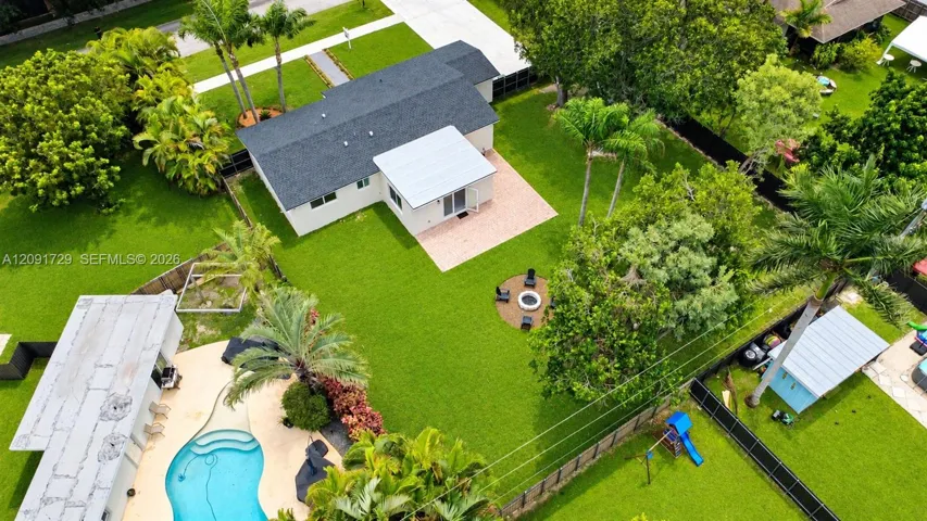 Expansive backyard featuring a paved patio, designated stone fire pit area, in-ground swimming pool with surrounding hardscaping, and mature landscaping
