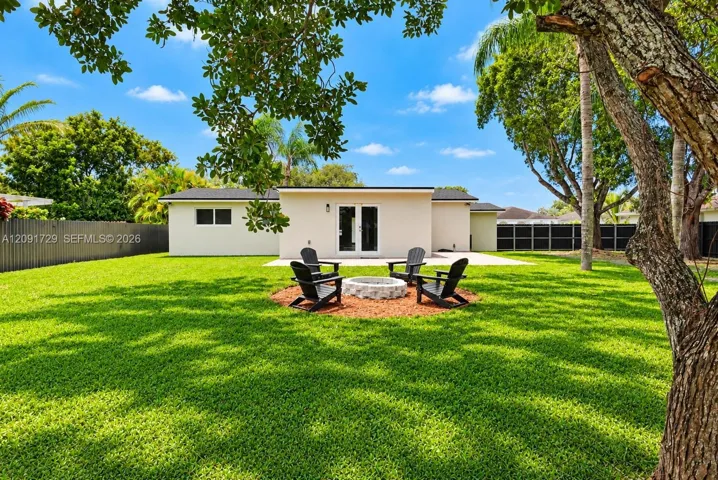 Expansive backyard featuring a stone-lined fire pit, concrete patio, perimeter privacy fencing, and mature trees