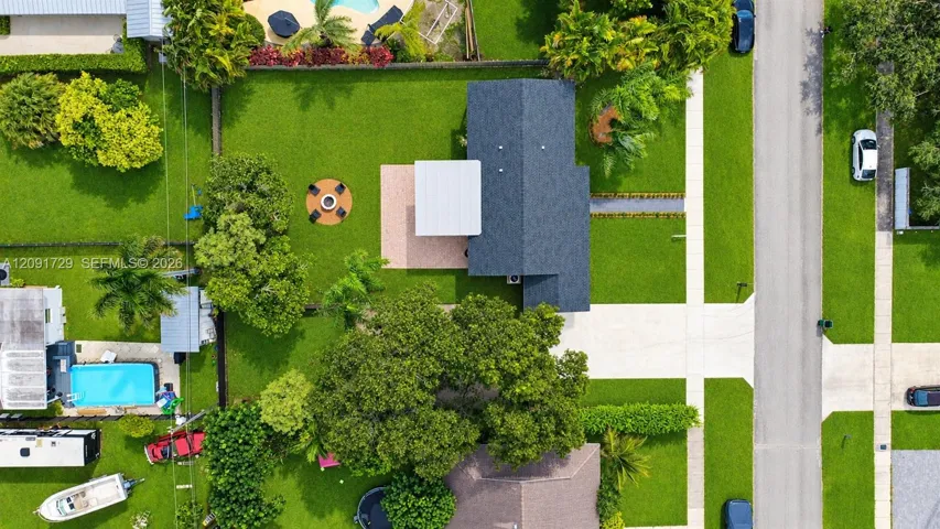 Aerial view of property featuring a sprawling lawn, a paved patio, a covered outdoor space, and a hardscaped fire pit area