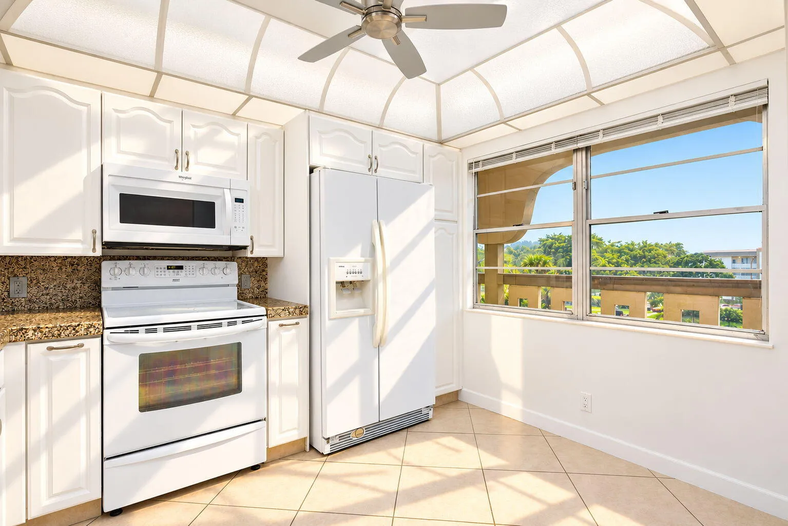 White cabinetry, tile flooring, built-in appliances, ample countertop space, and a ceiling fan