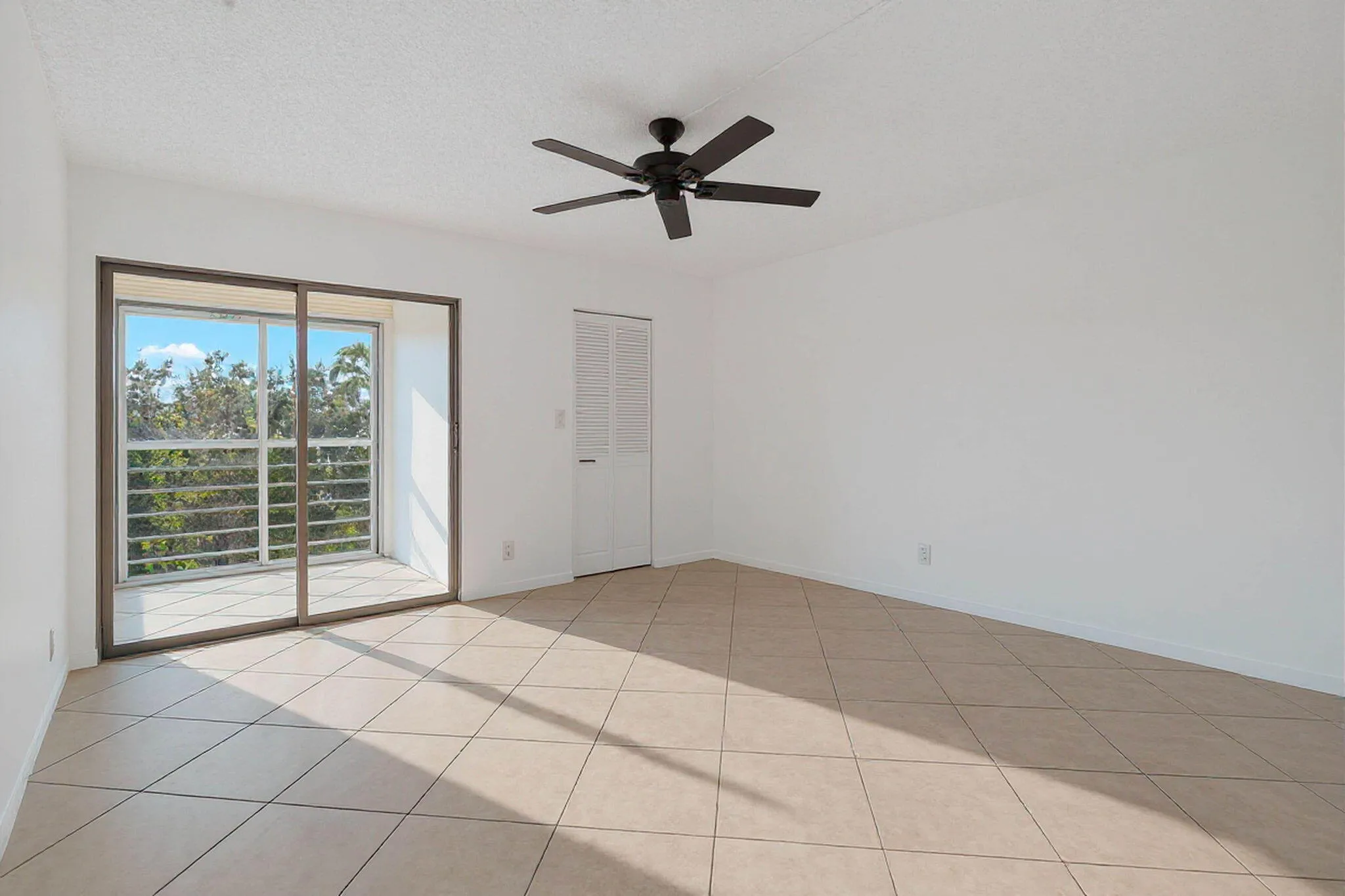Expansive room with large format tile flooring, white walls, and a ceiling fan
