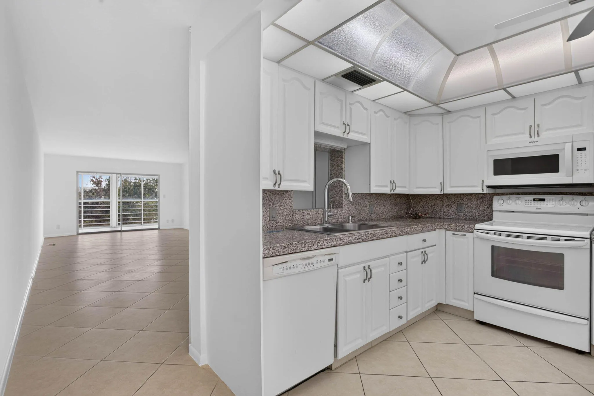 White kitchen cabinetry with integrated white appliances, L-shaped countertop, and tile flooring