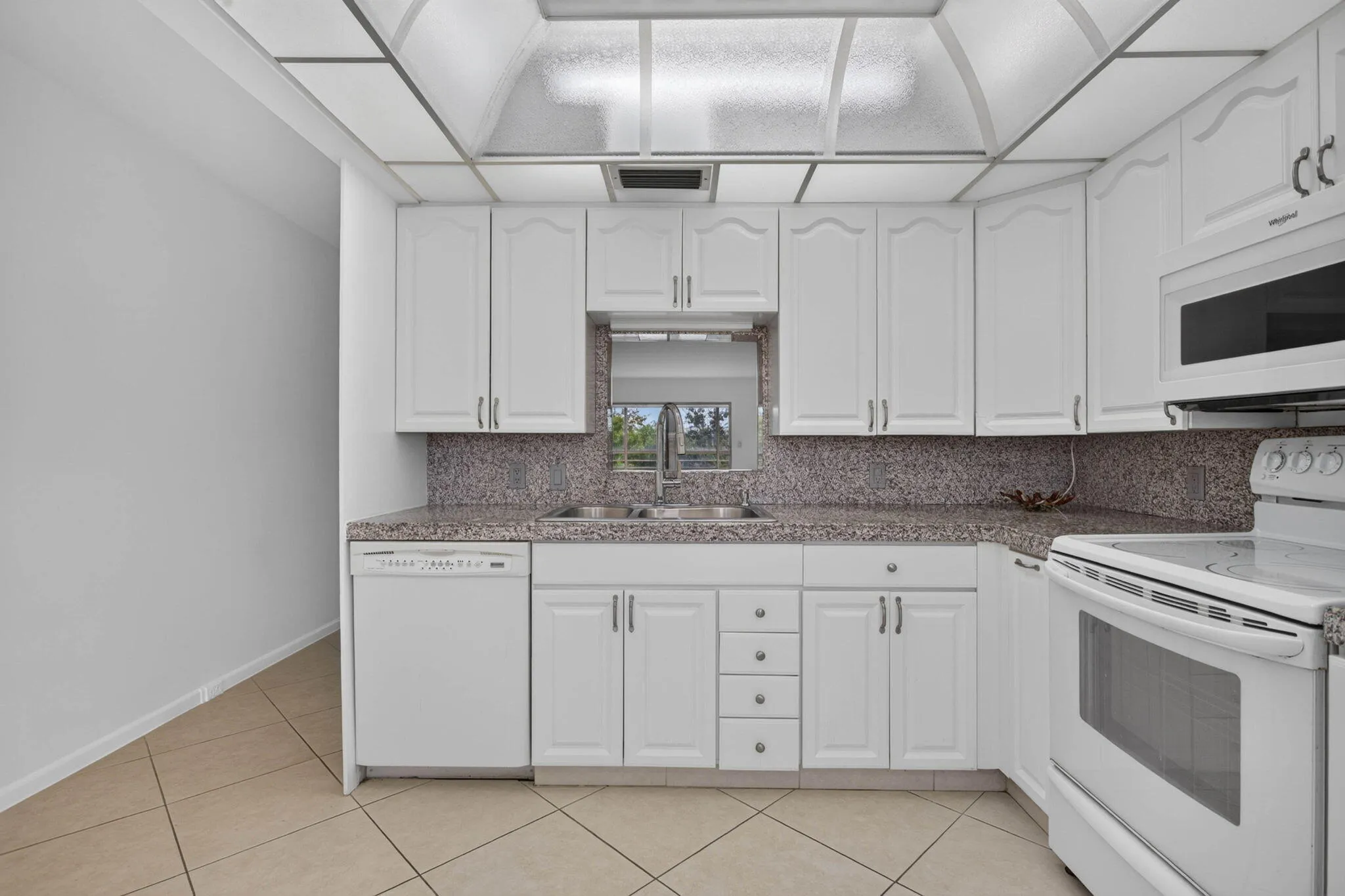 Kitchen featuring white cabinetry, solid surface countertops, tile flooring, and integrated white appliances