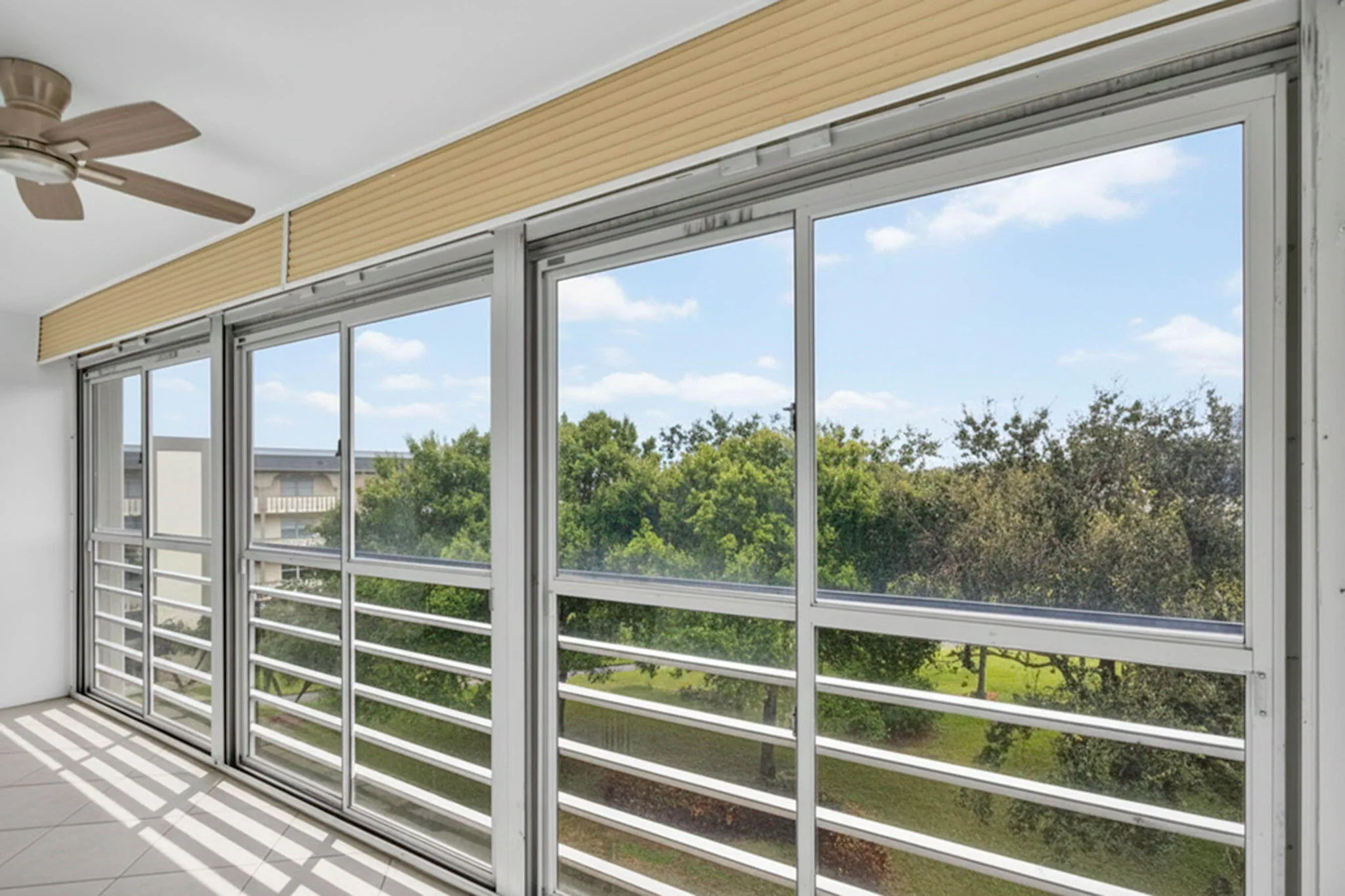 Multiple floor-to-ceiling windows, sliding glass door access, exterior safety bars, and an overhead ceiling fan