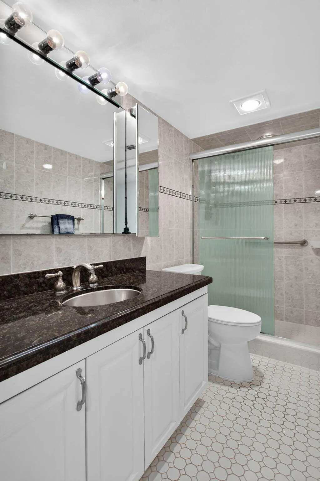 White vanity with a dark stone-finish countertop and undermount sink