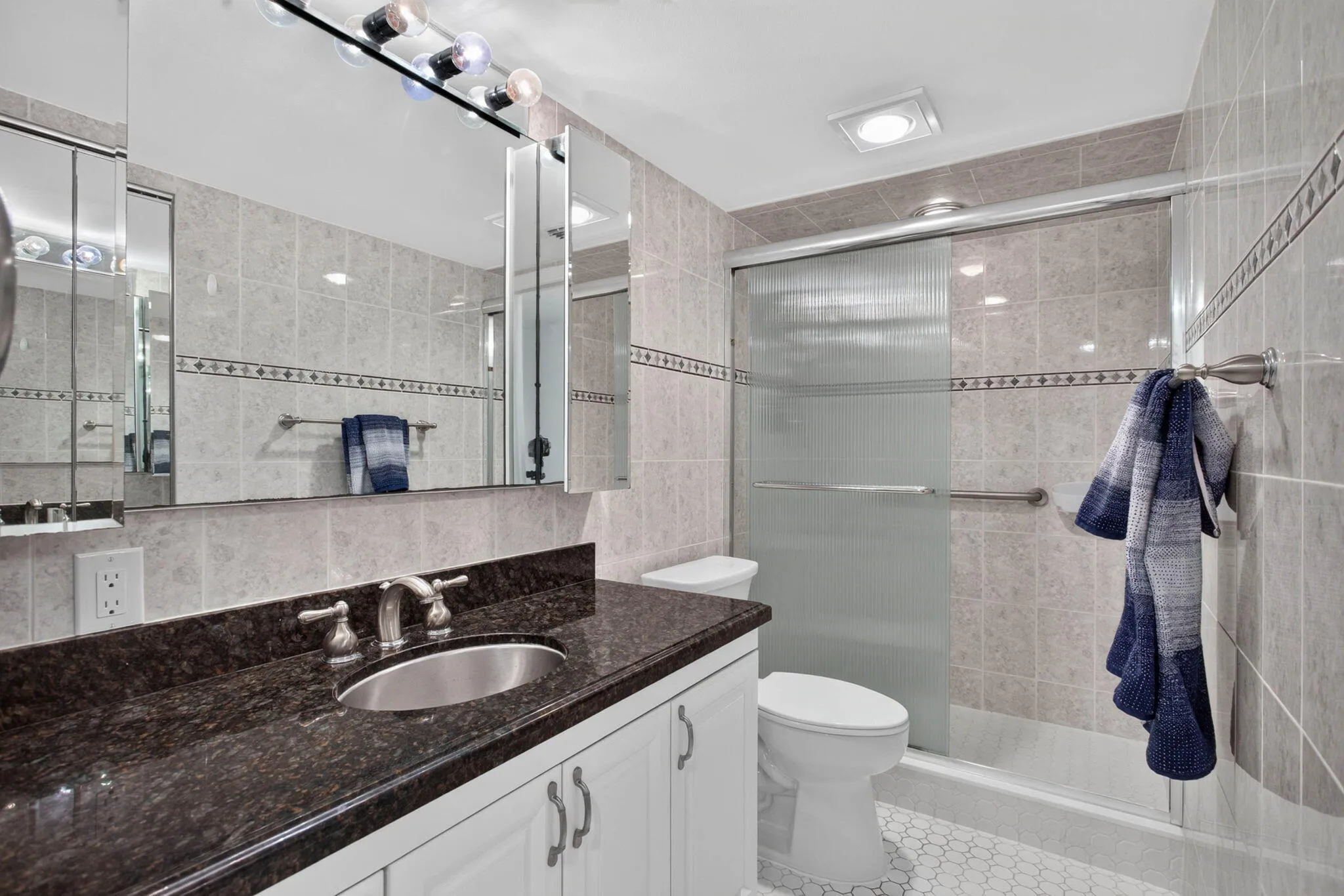 Vanity with a dark polished countertop, undermount sink, and brushed nickel faucet