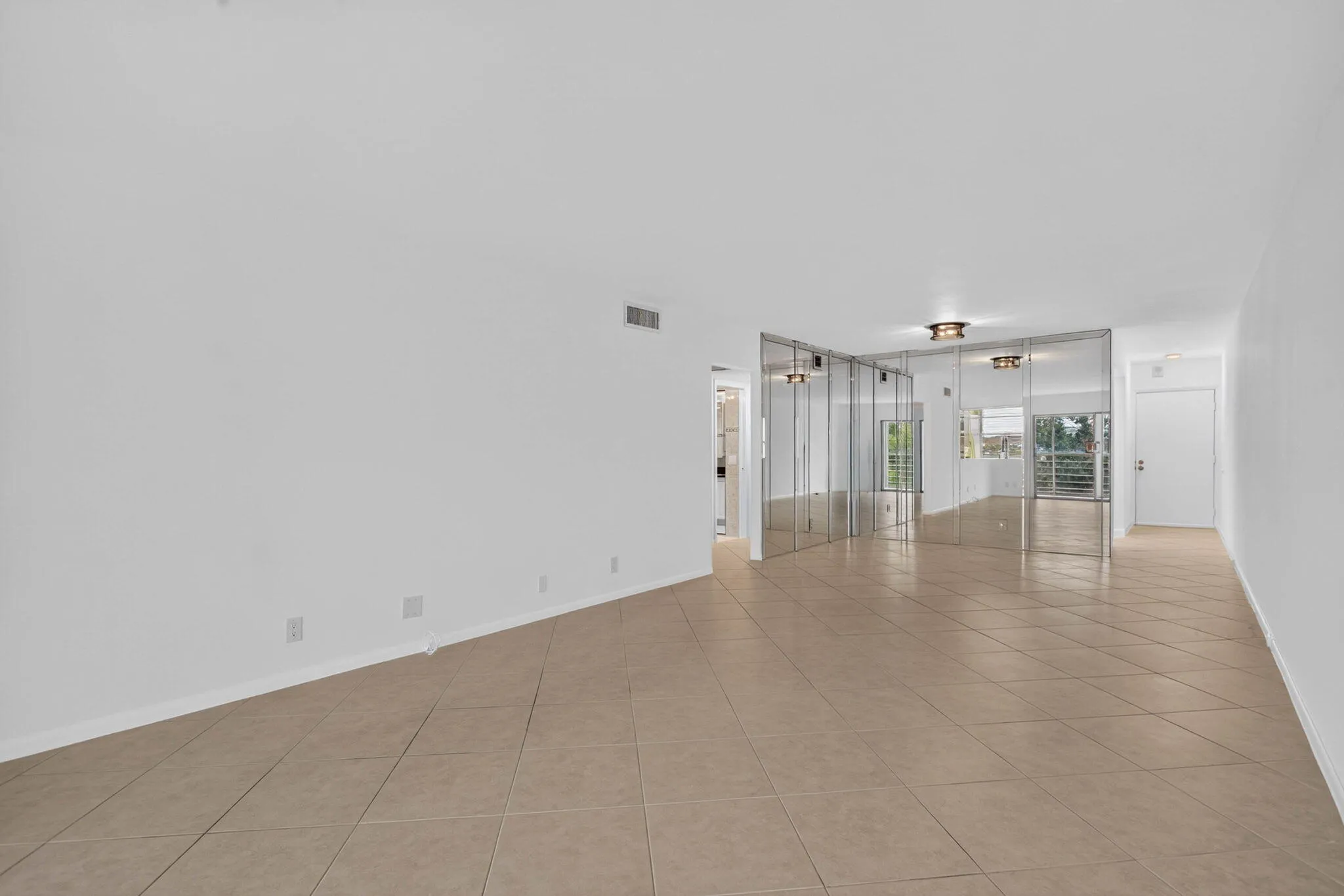 Expansive room with neutral tile flooring, white walls, mirror paneling, and a flush mount ceiling fixture