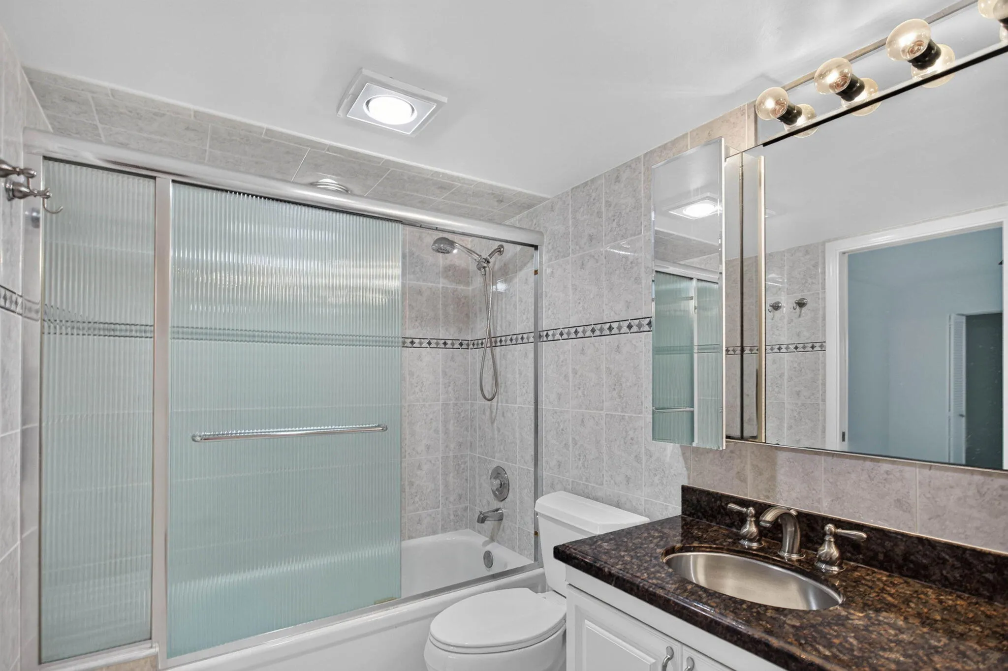 Bathroom featuring a vanity with an undermount sink, a dark countertop, a mirrored medicine cabinet, a full bathtub, and a shower with sliding glass doors