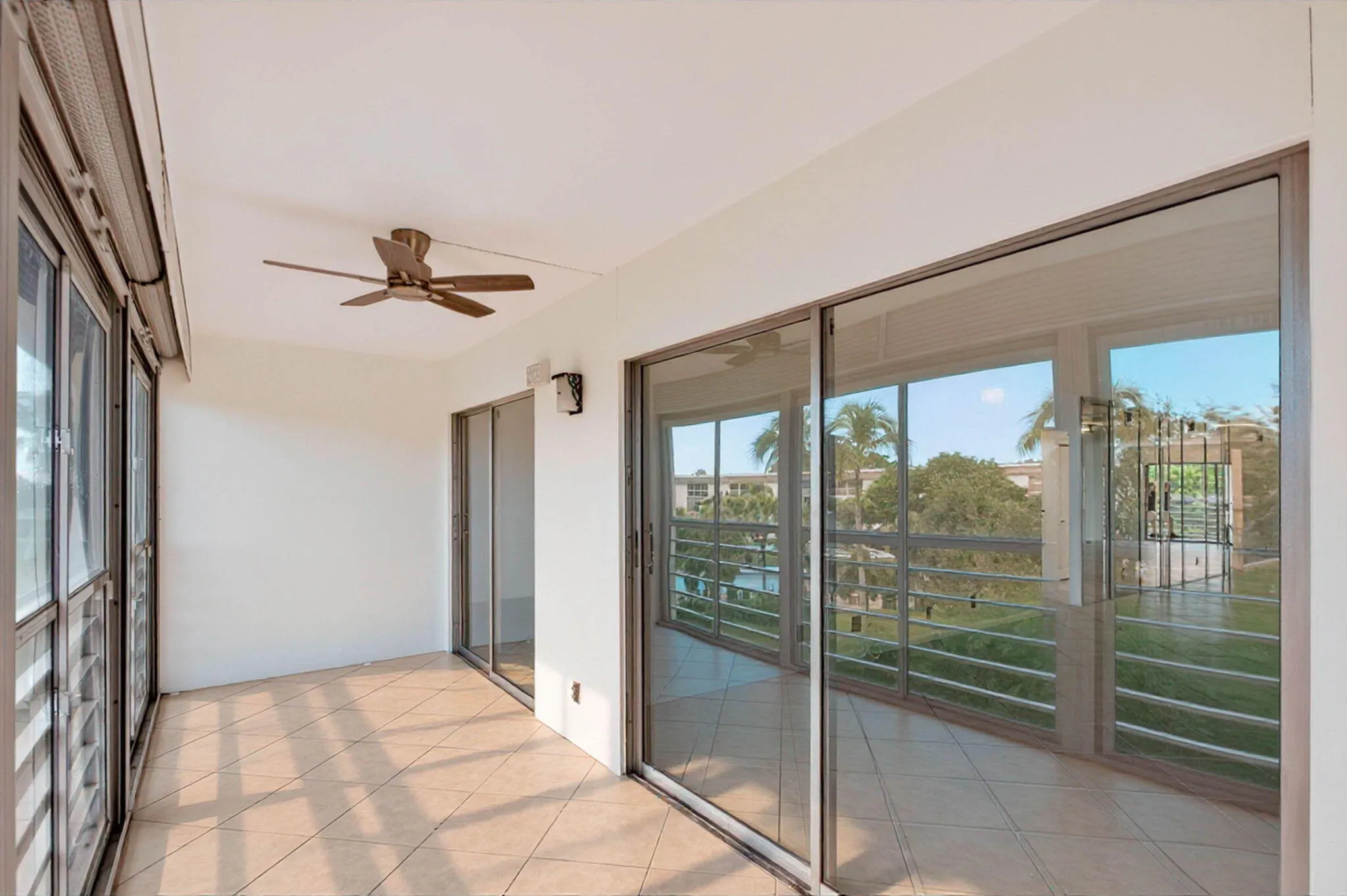 Tiled outdoor space featuring a ceiling fan, multiple sliding glass doors, and a metal railing