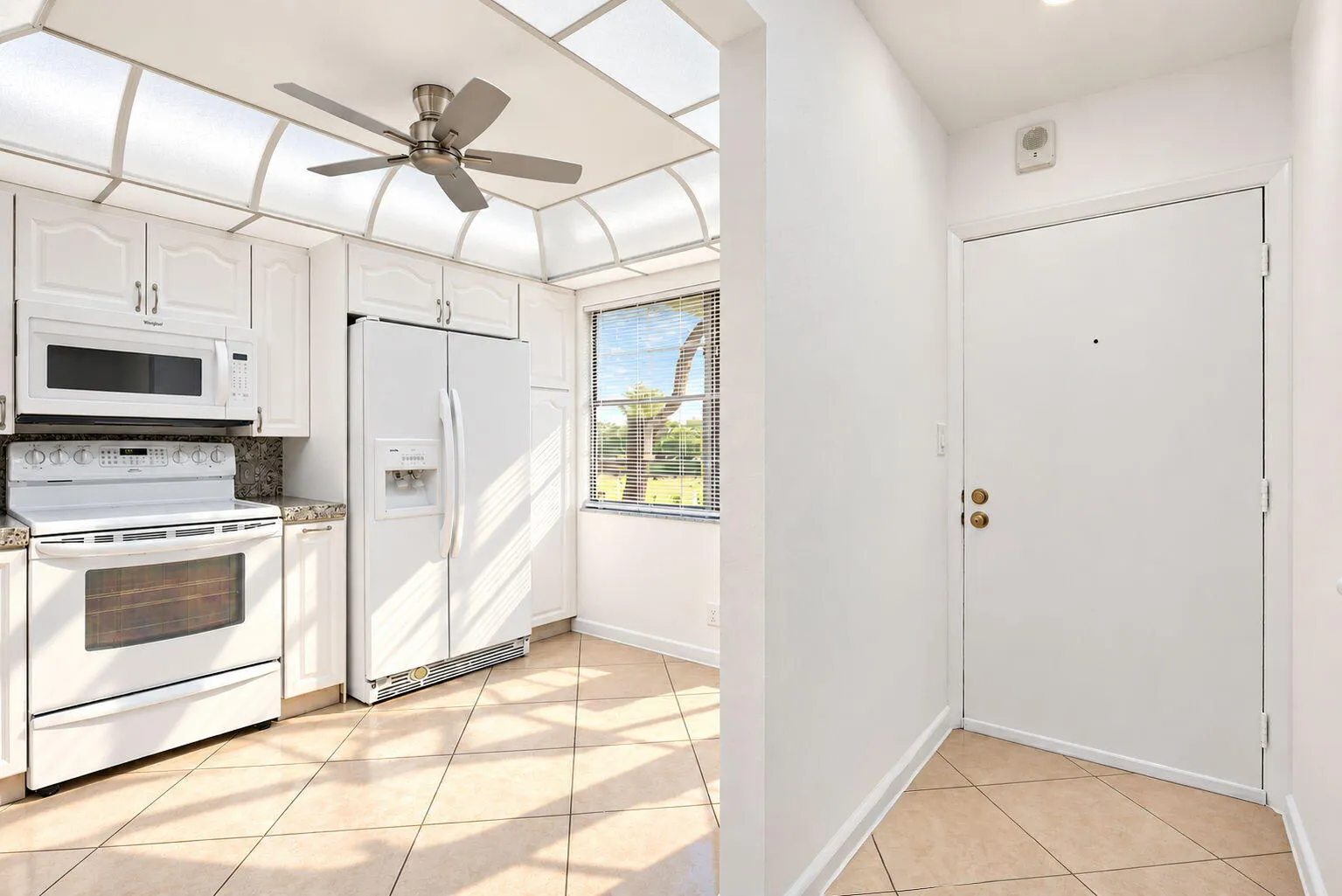 White kitchen cabinetry, full suite of white appliances, tiled flooring, natural lighting, and a ceiling fan with integrated lighting