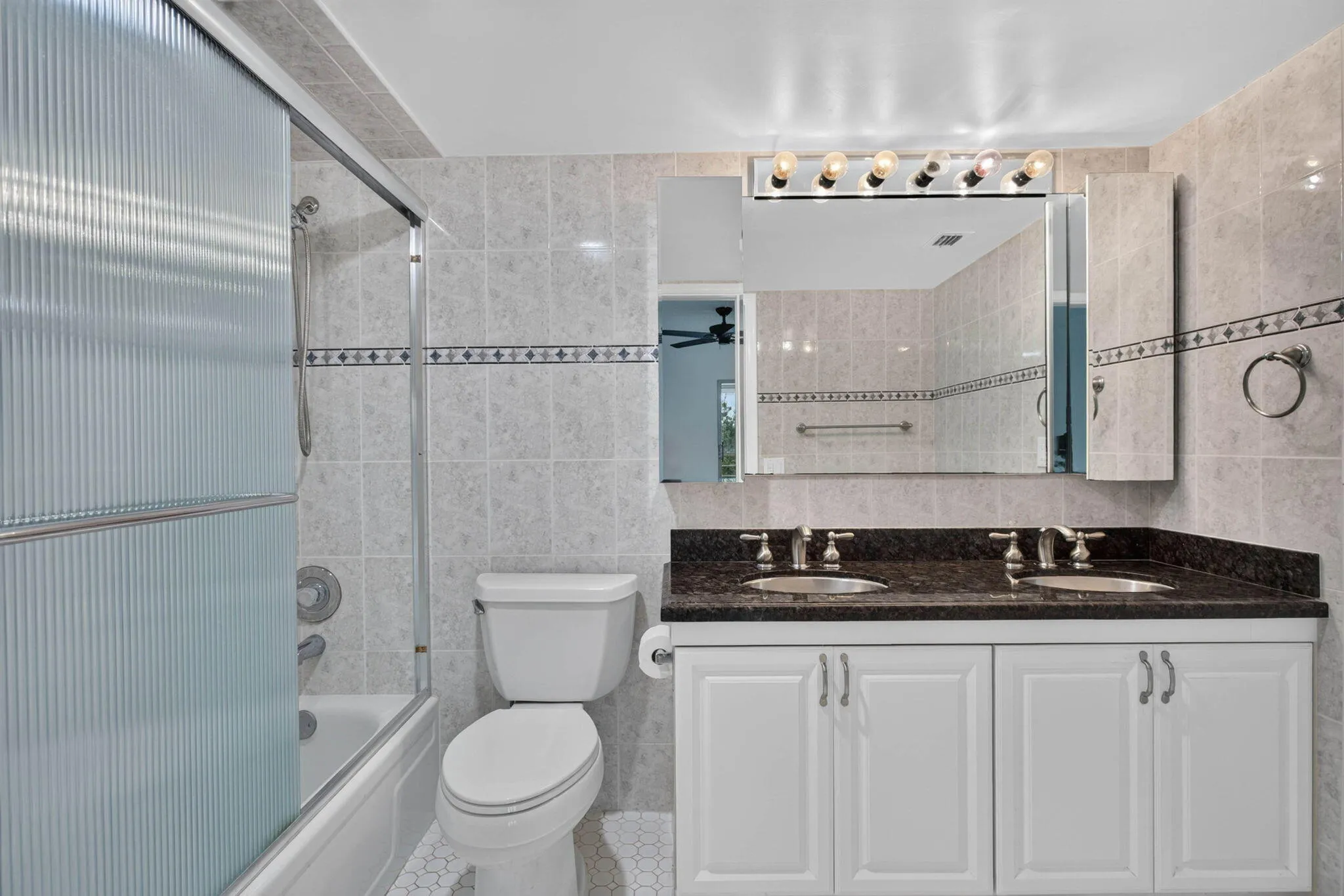 Dual vanity with dark stone countertop, white cabinetry, and polished chrome fixtures