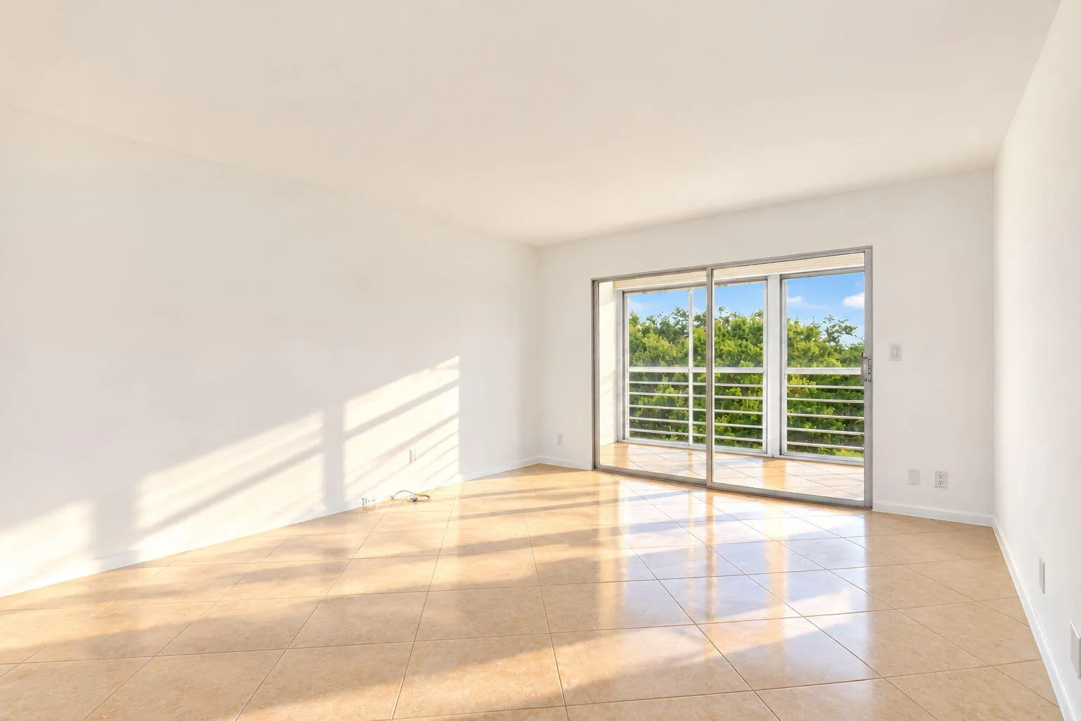 Sliding glass doors opening to a balcony with metal railings, tile flooring, and white painted walls