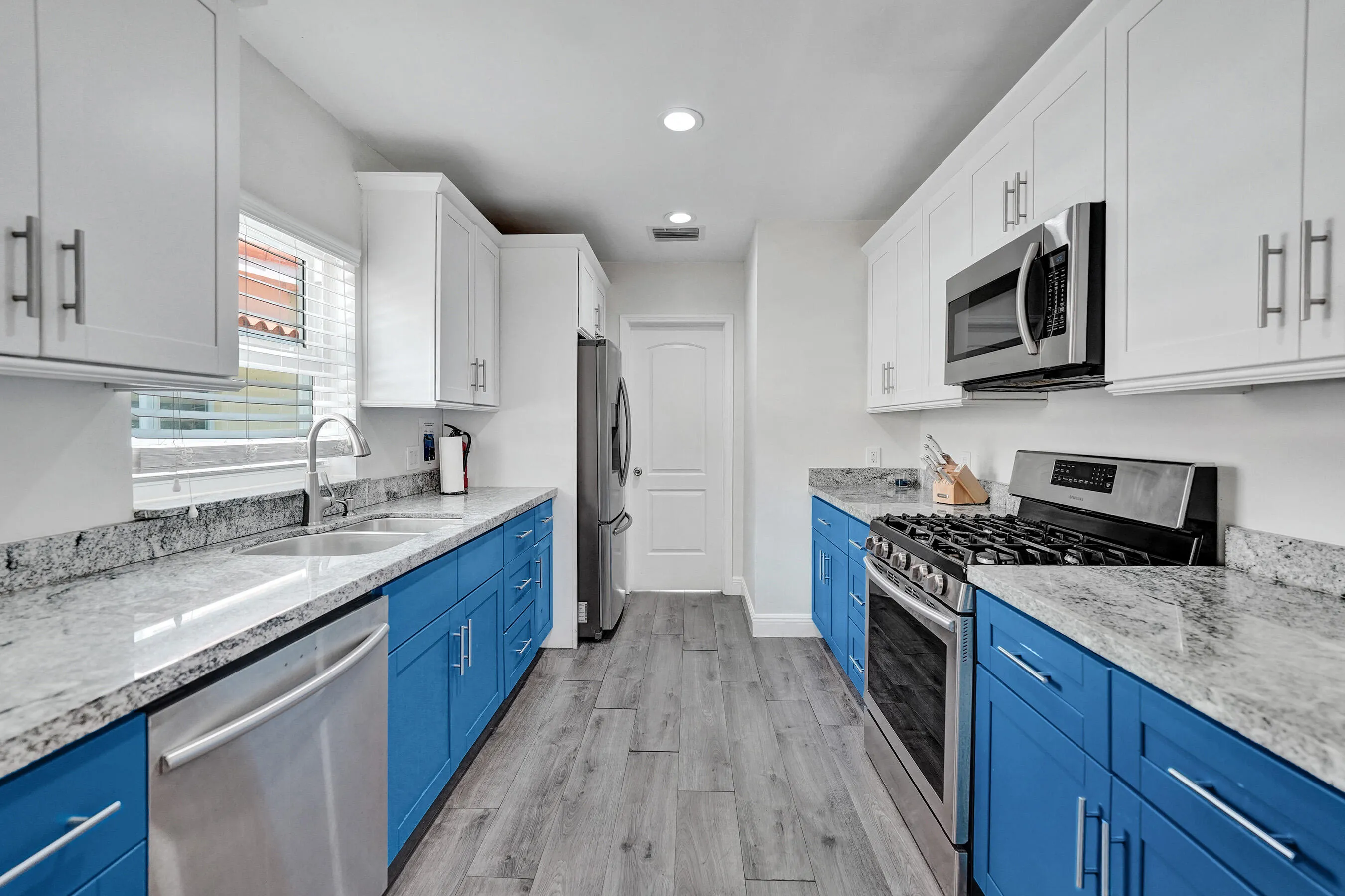 Kitchen featuring light-toned countertops, contrasting blue and white cabinetry, stainless steel appliances, and wood-finish flooring