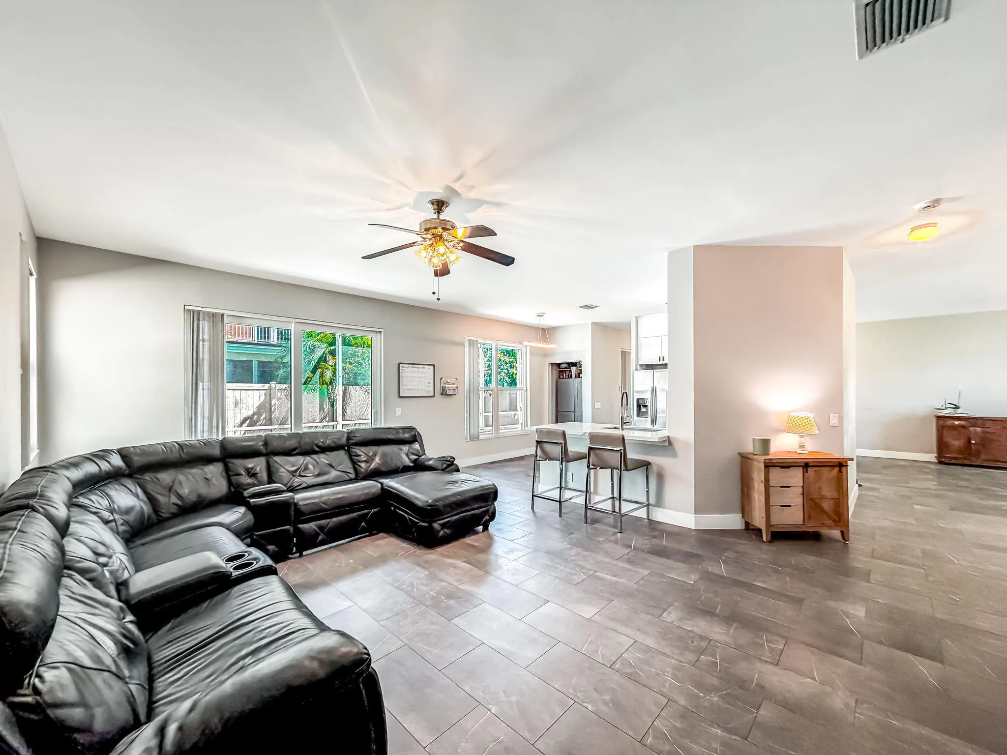 Expansive great room featuring large format tile flooring, a ceiling fan with integrated lighting, and multiple windows