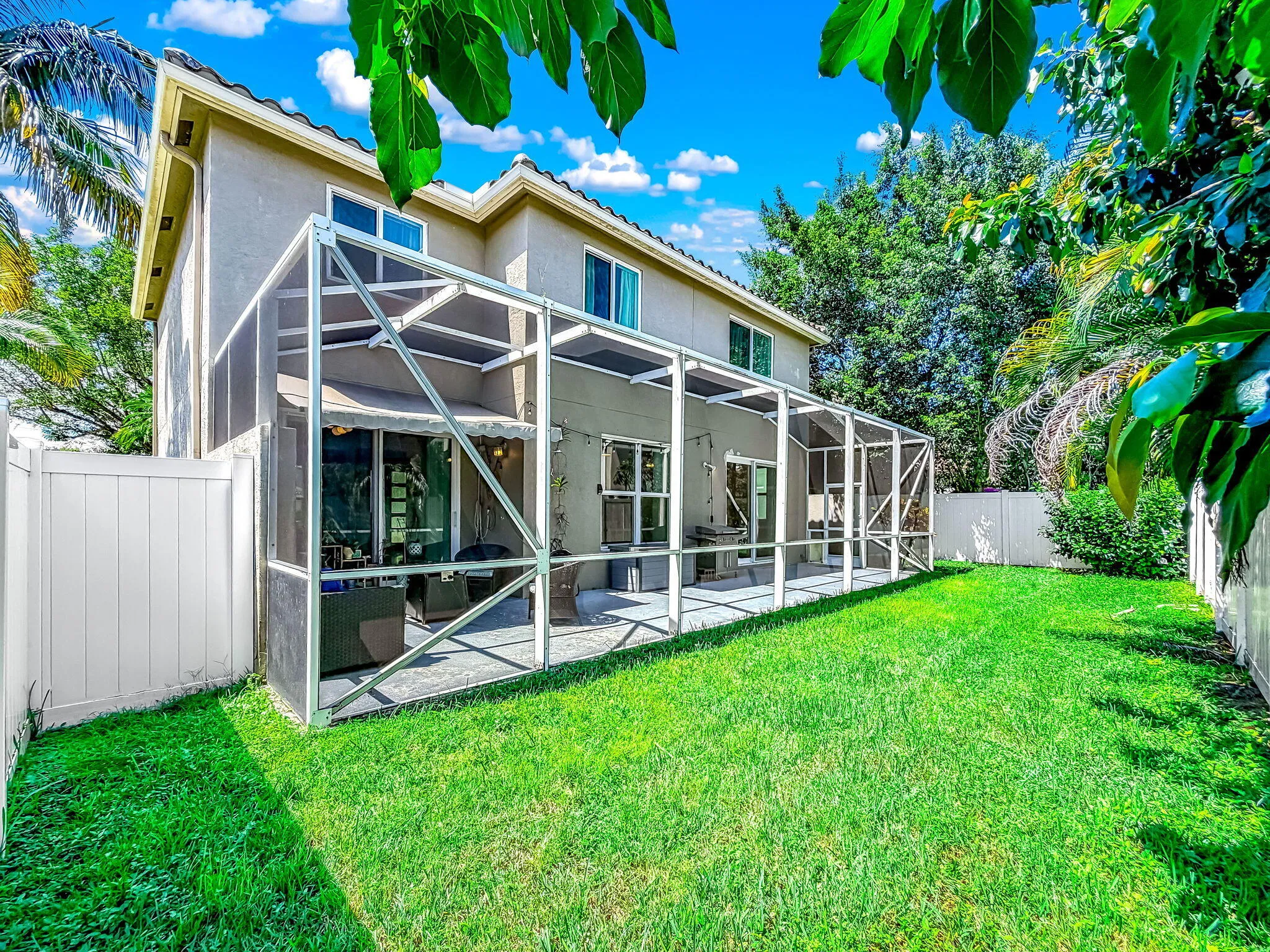 Expansive grass lawn with a screened patio, white privacy fencing, and mature trees
