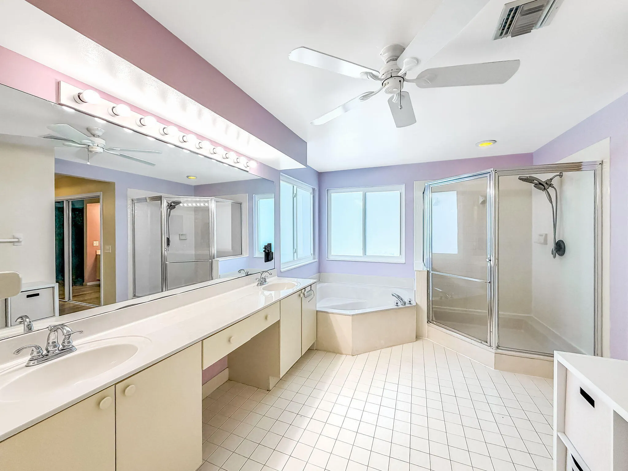 Dual vanity with integrated sinks, corner soaking tub, glass-enclosed shower, and ceiling fan