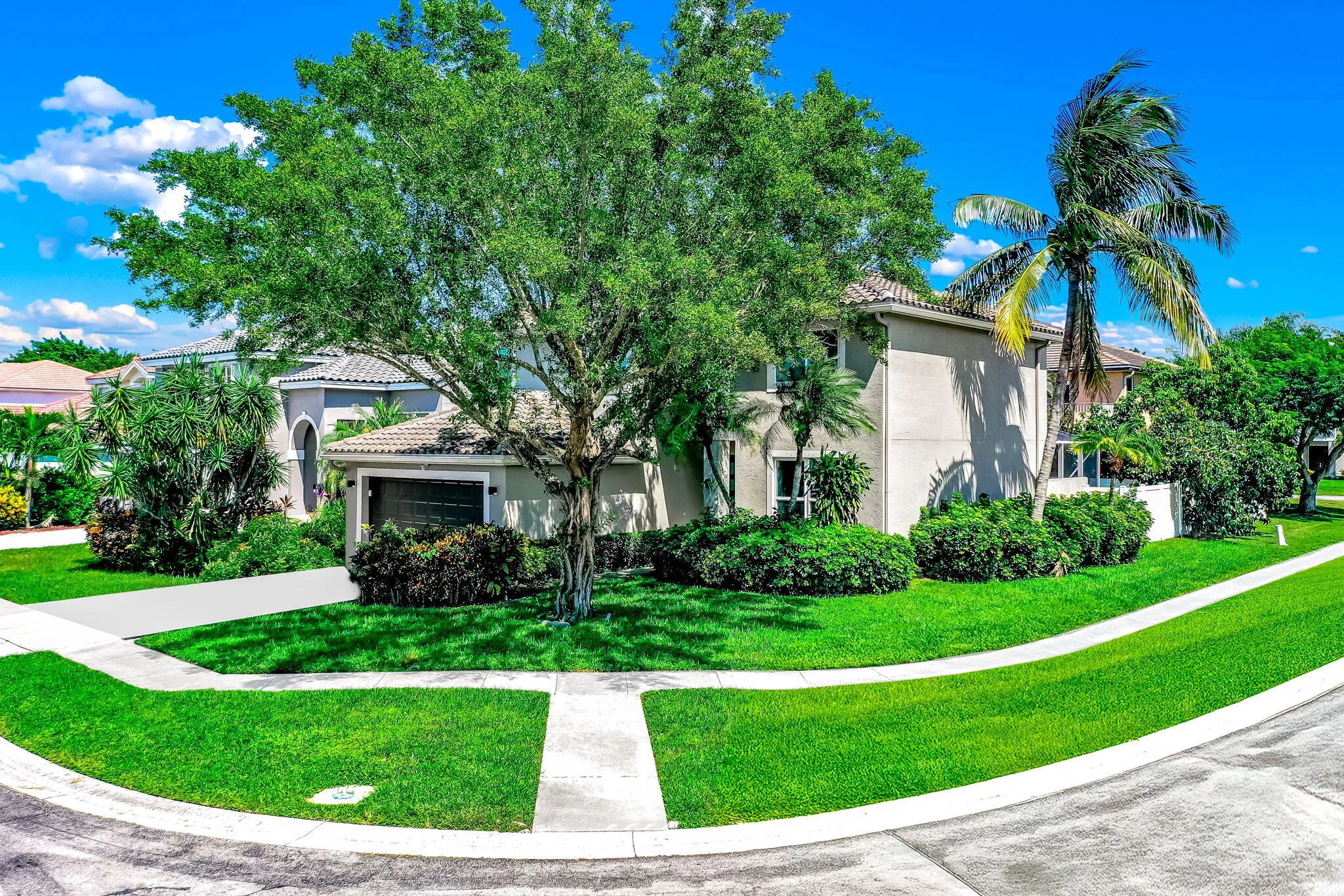 Stucco exterior with a tile roof, an integrated garage, a concrete driveway, and established landscaping