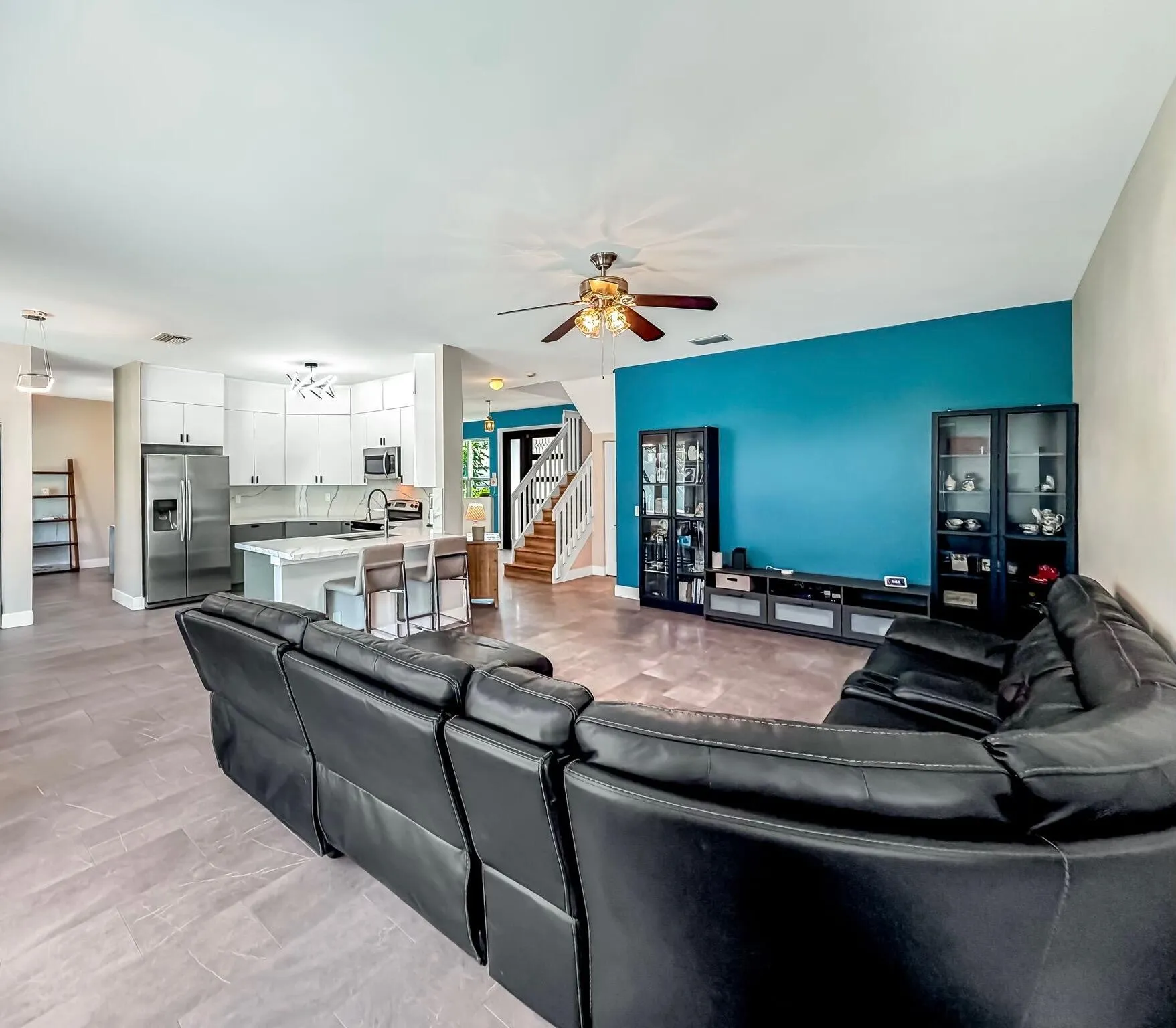 Expansive great room featuring large format tile flooring, a ceiling fan with integrated lighting, and multiple windows
