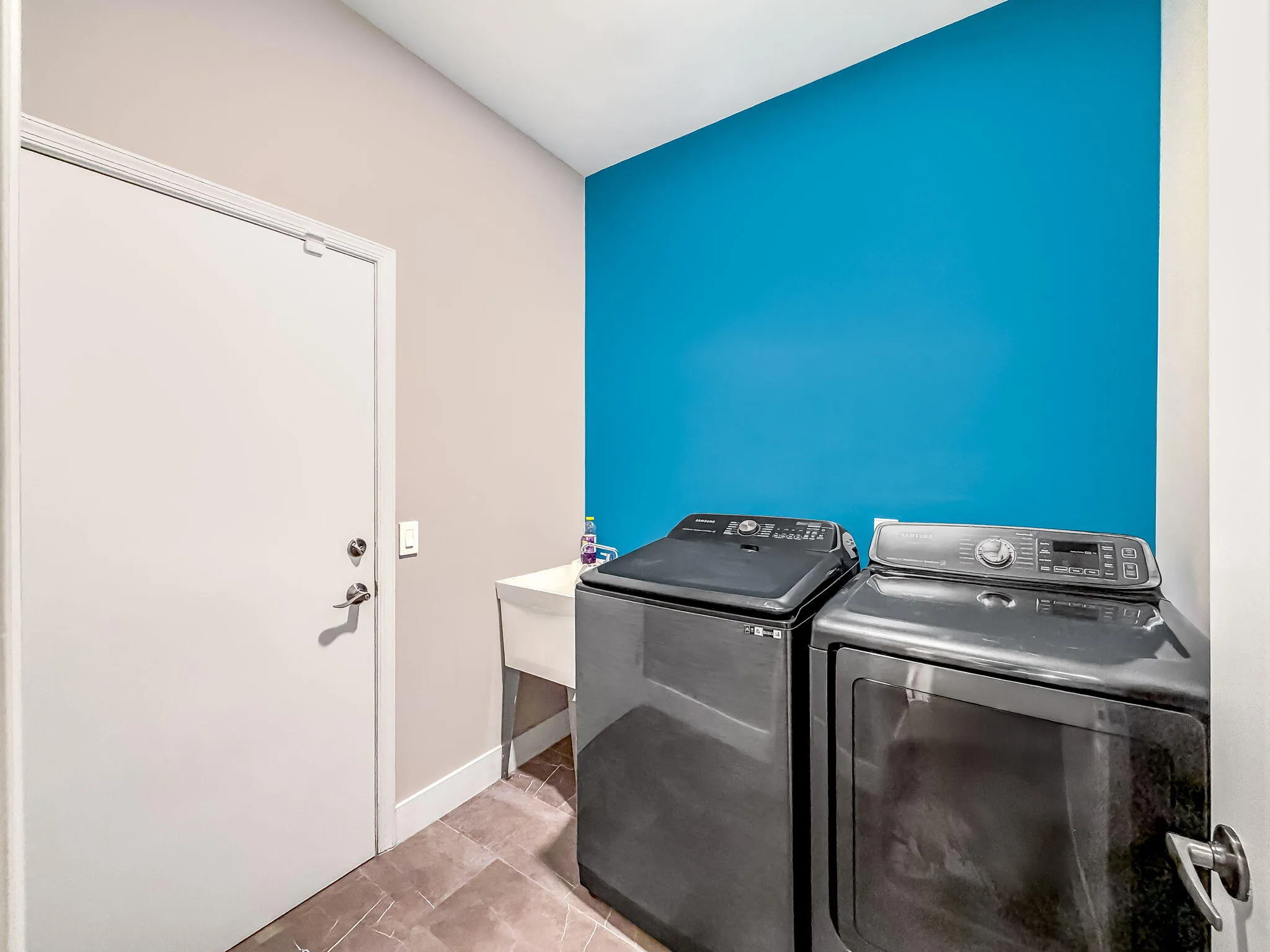 Laundry area featuring a utility sink, tiled flooring, and a vibrant accent wall