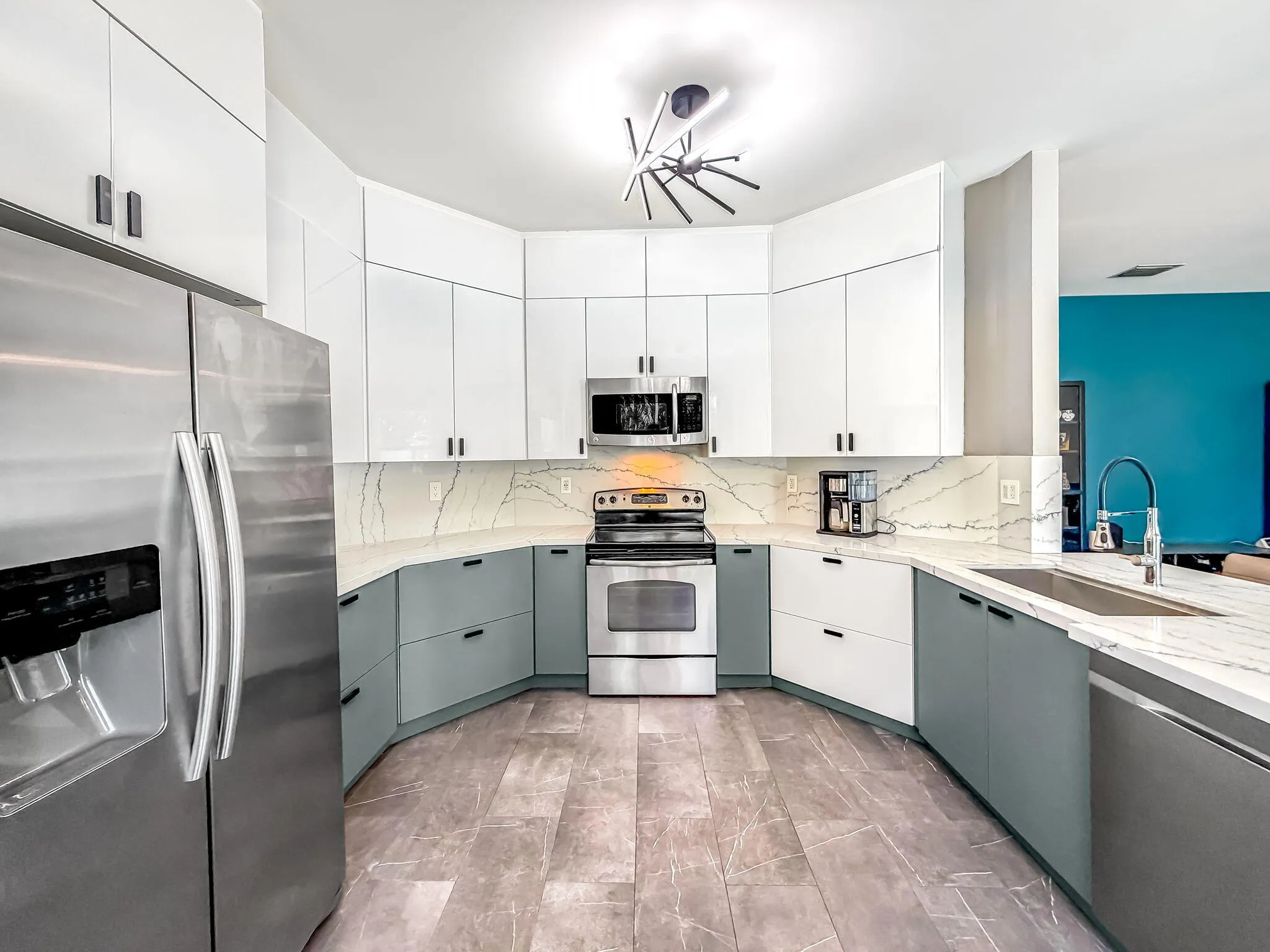 Curved kitchen featuring stainless steel appliances, two-tone cabinetry, a decorative ceiling light fixture, and an undermount sink