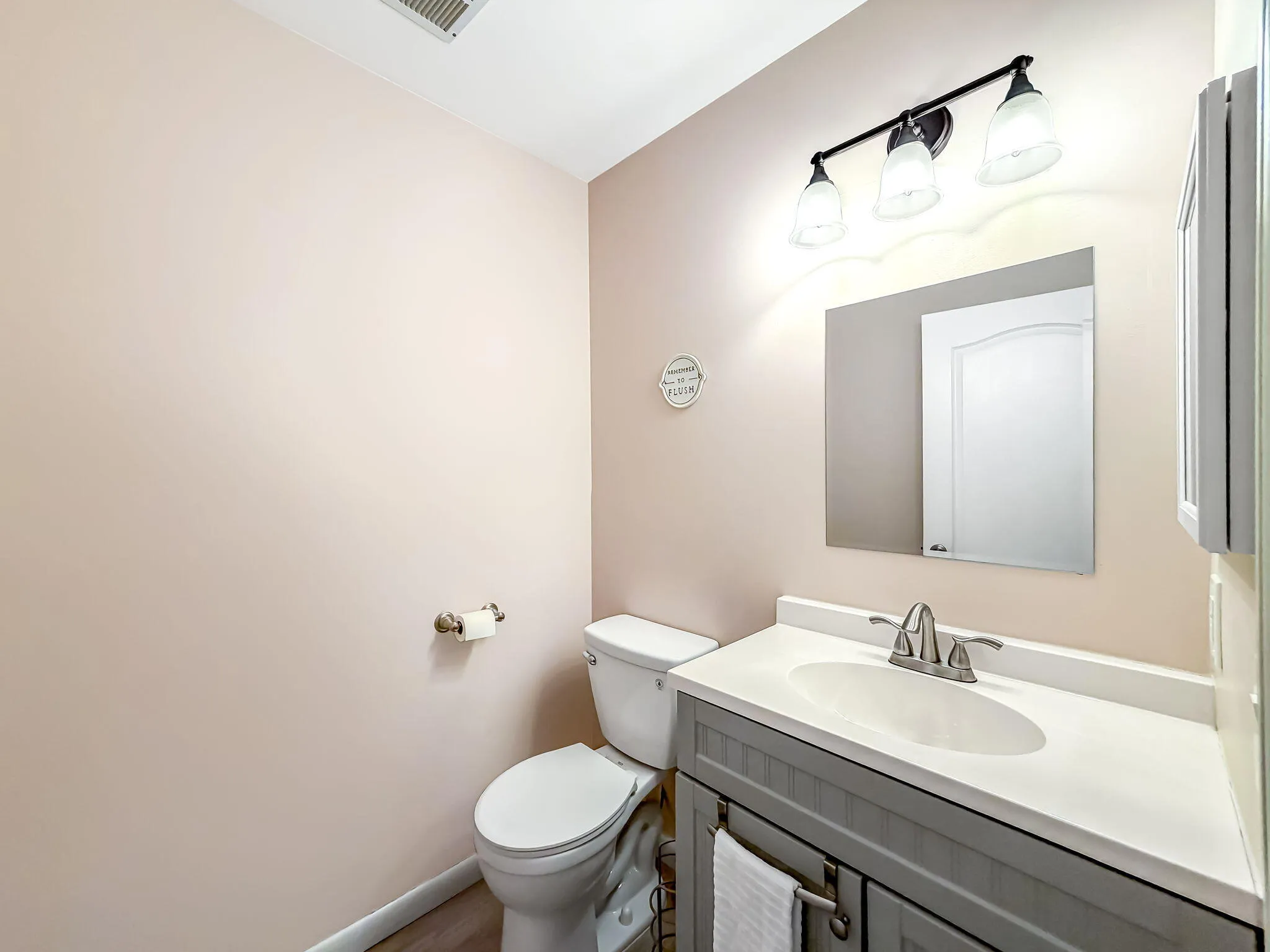 Gray vanity with a white countertop and integrated sink, chrome-finish faucet, and a wall-mounted mirror