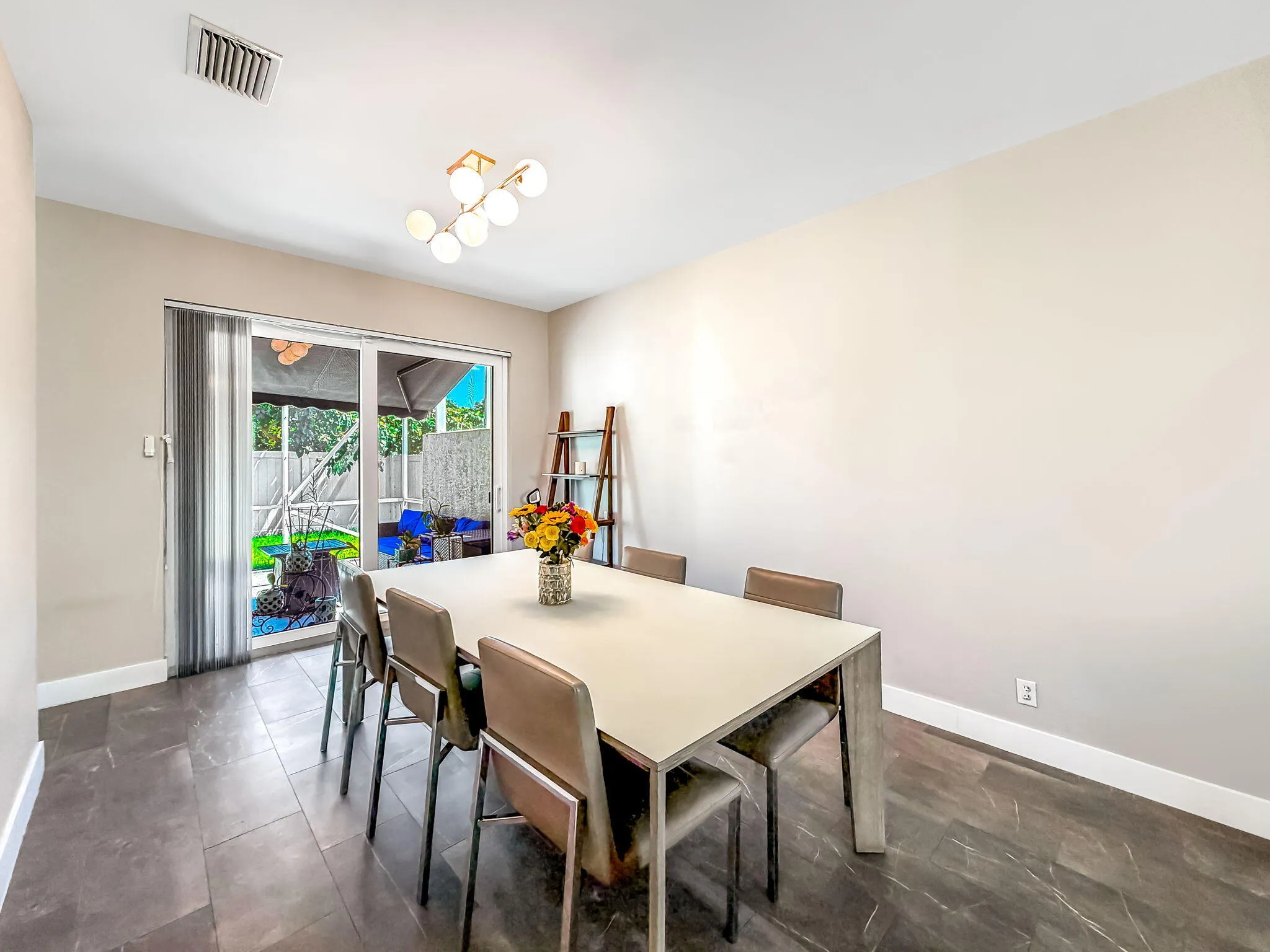 Sliding glass door, contemporary linear chandelier, dark tile flooring, built-in shelving, and white baseboards
