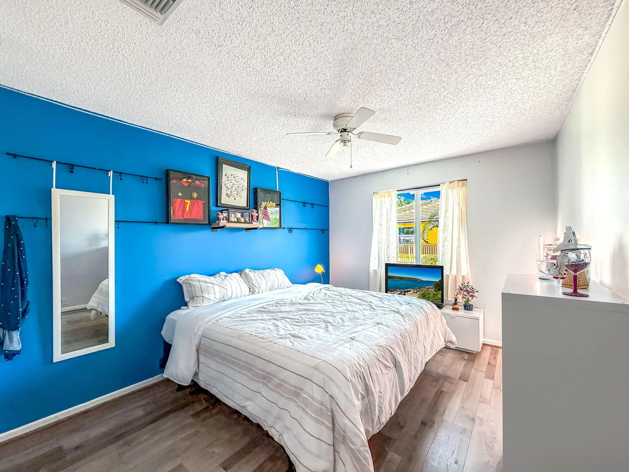 Wood-finish flooring, ceiling fan with integrated lighting, and a window with white curtains