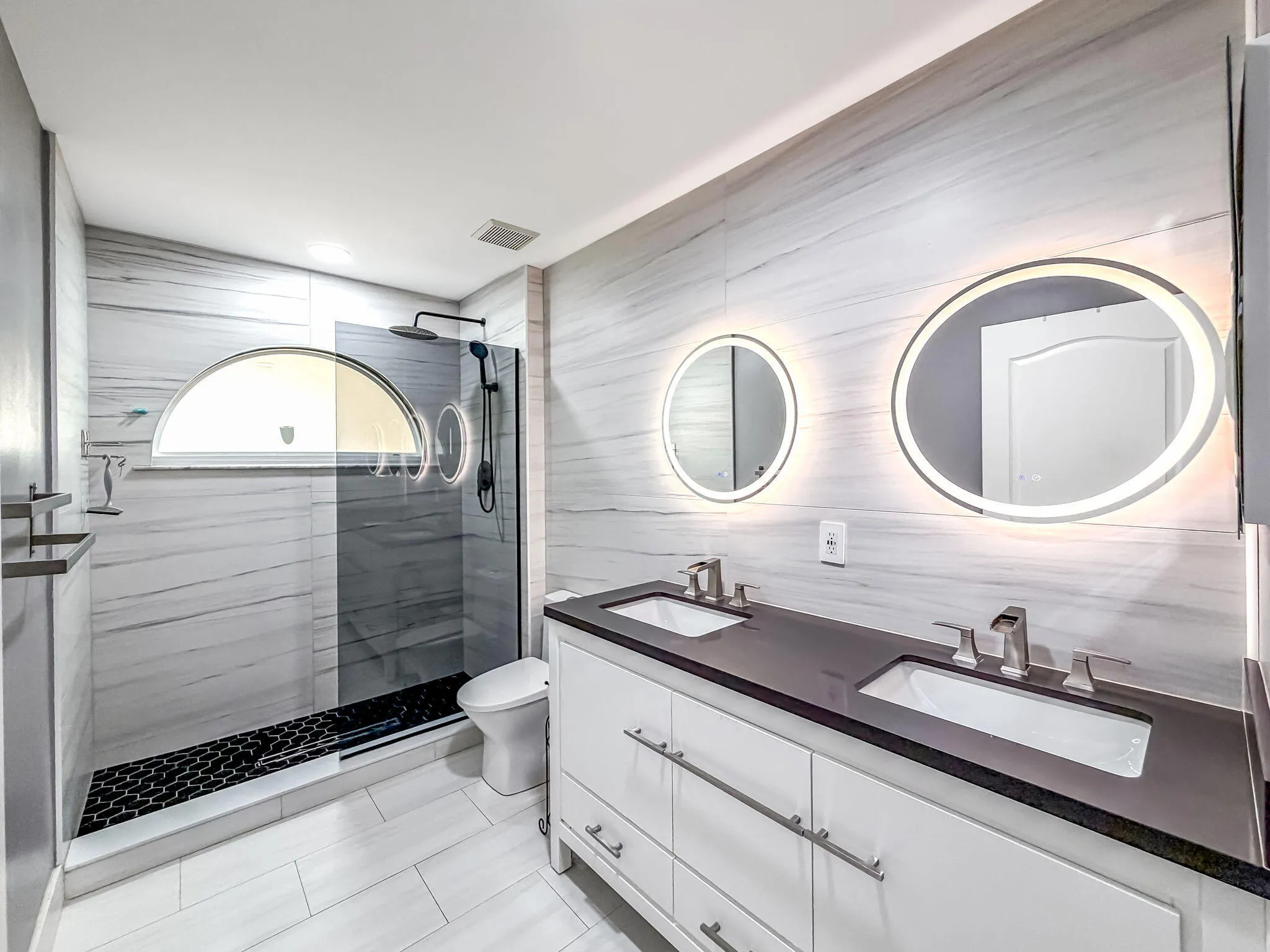 Dual vanity with undermount sinks, stone countertop, and illuminated round mirrors