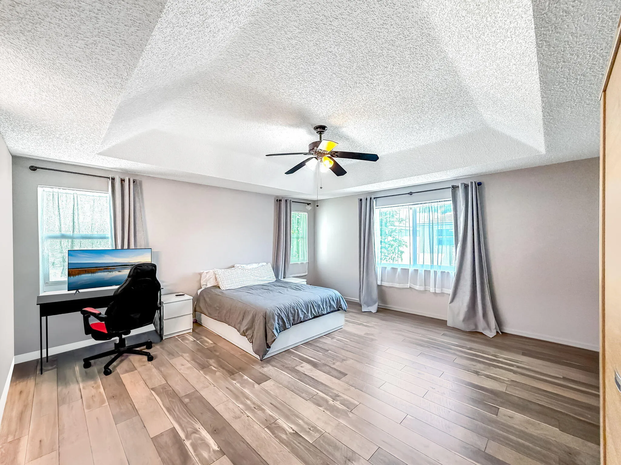 Tray ceiling with integrated lighting, wood-finish flooring, and multiple windows