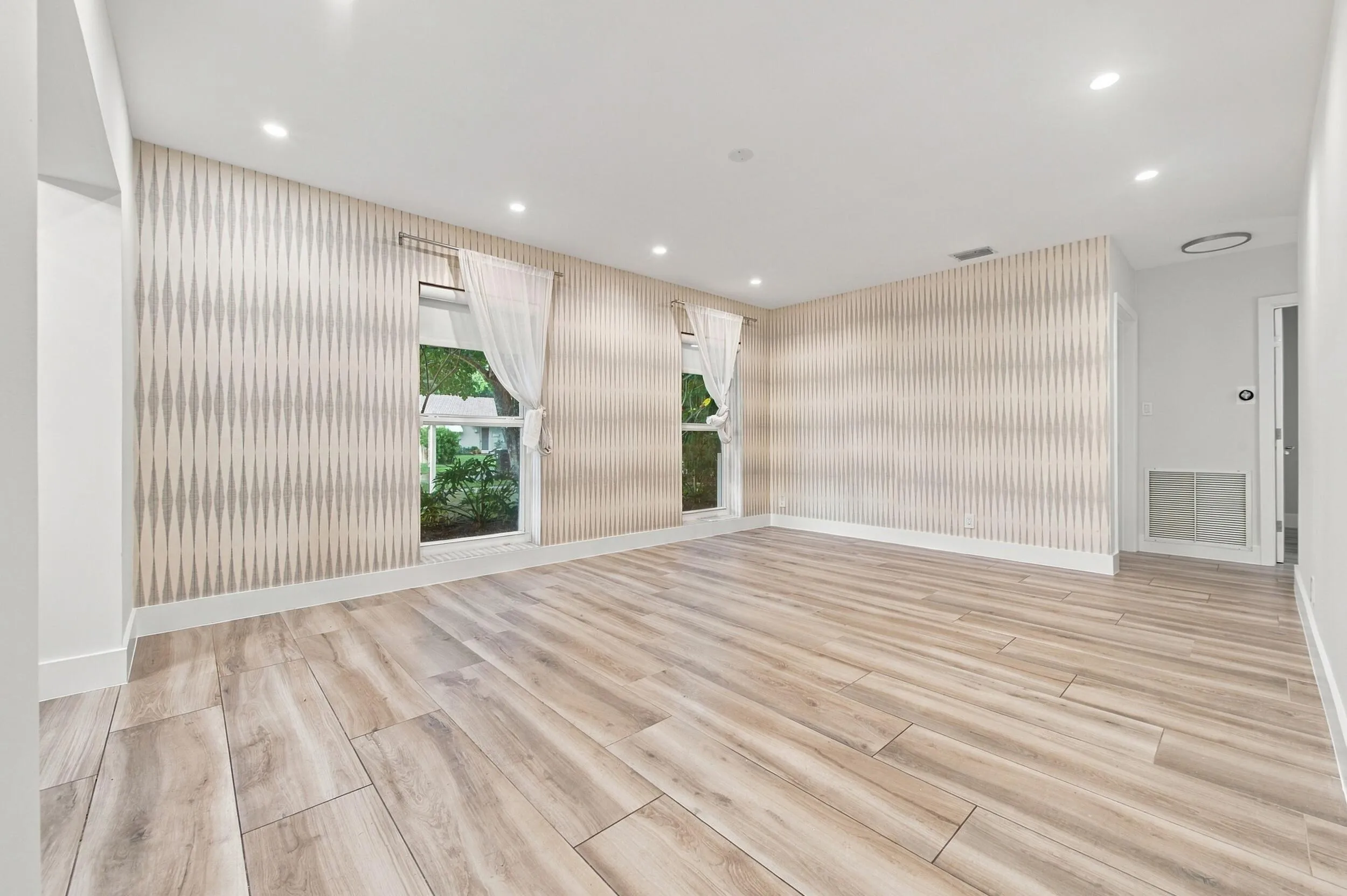 Light wood-finish flooring, recessed ceiling lighting, patterned accent wall, and two windows