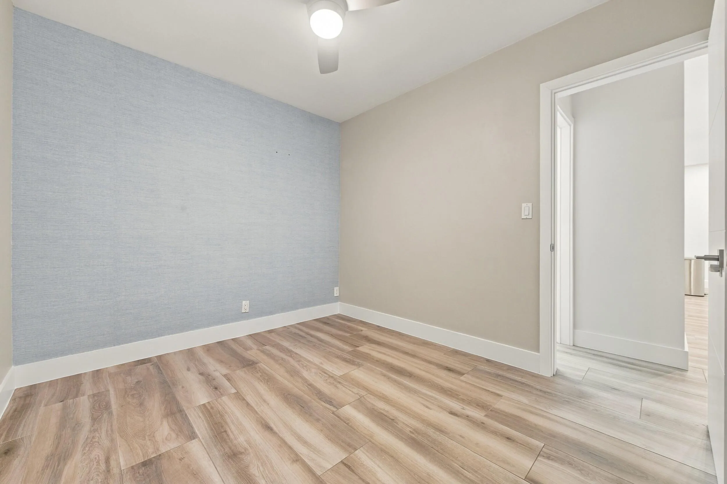 Wood-finish flooring, accent wall with textured wallcovering, ceiling fan, and white trim throughout