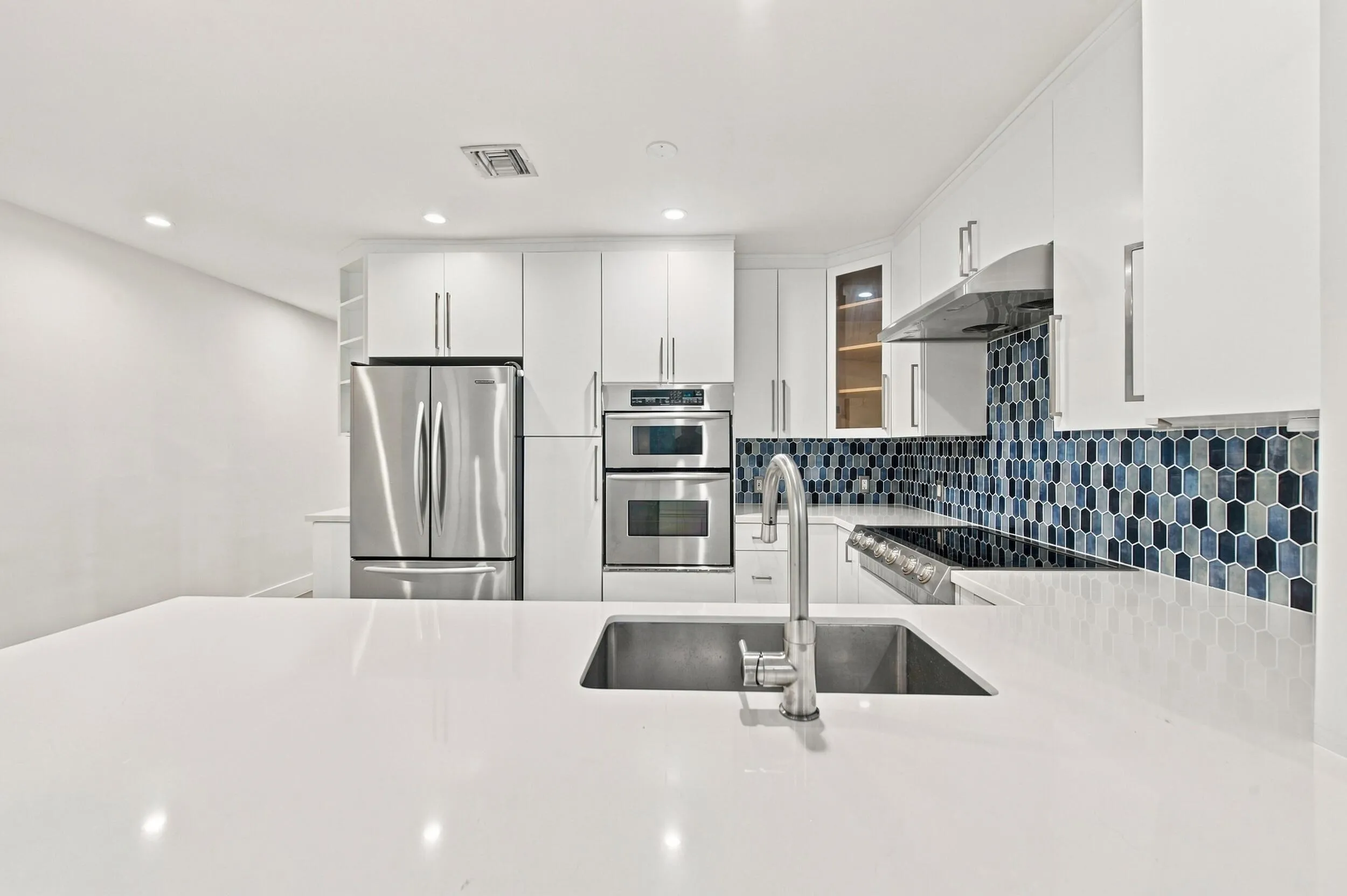 Kitchen featuring a large island with an undermount sink, stainless steel appliances, white cabinetry, and a patterned tile backsplash