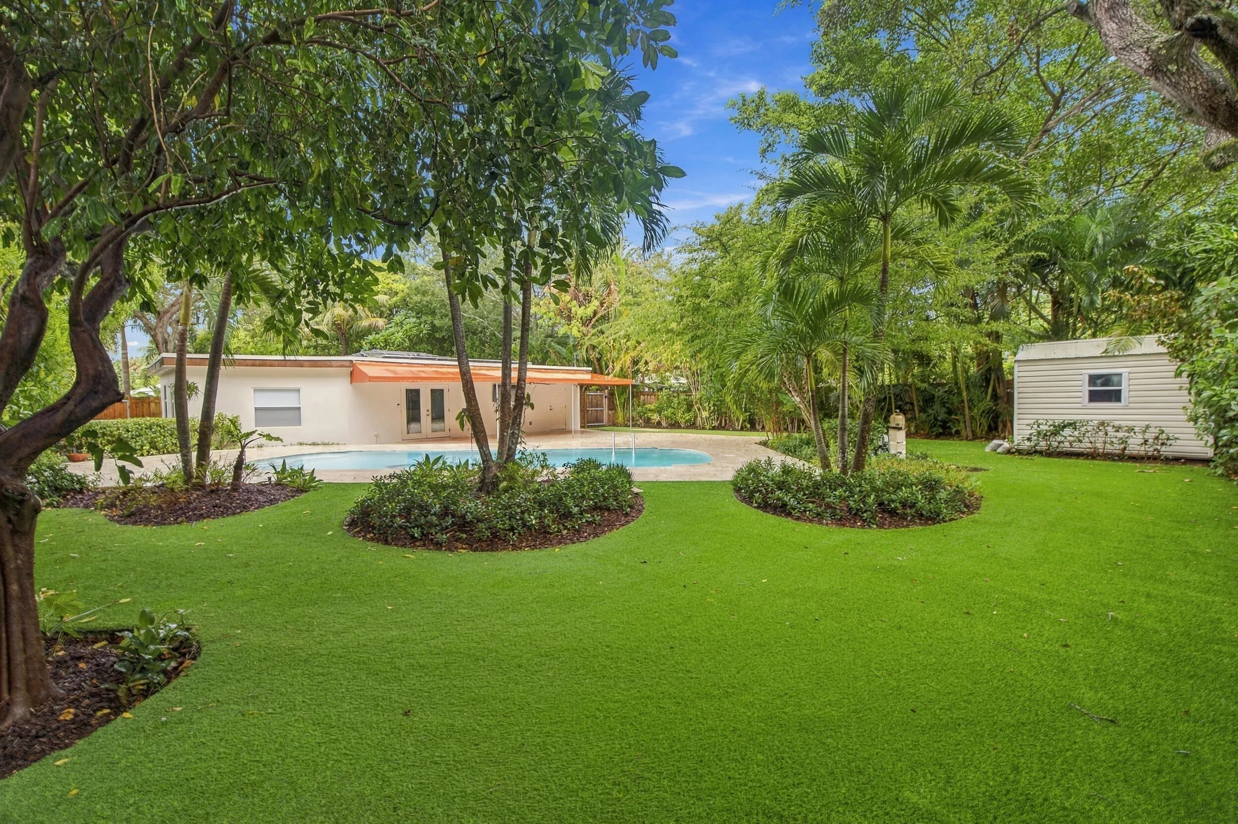 Expansive artificial turf lawn with sculpted garden beds and mature trees