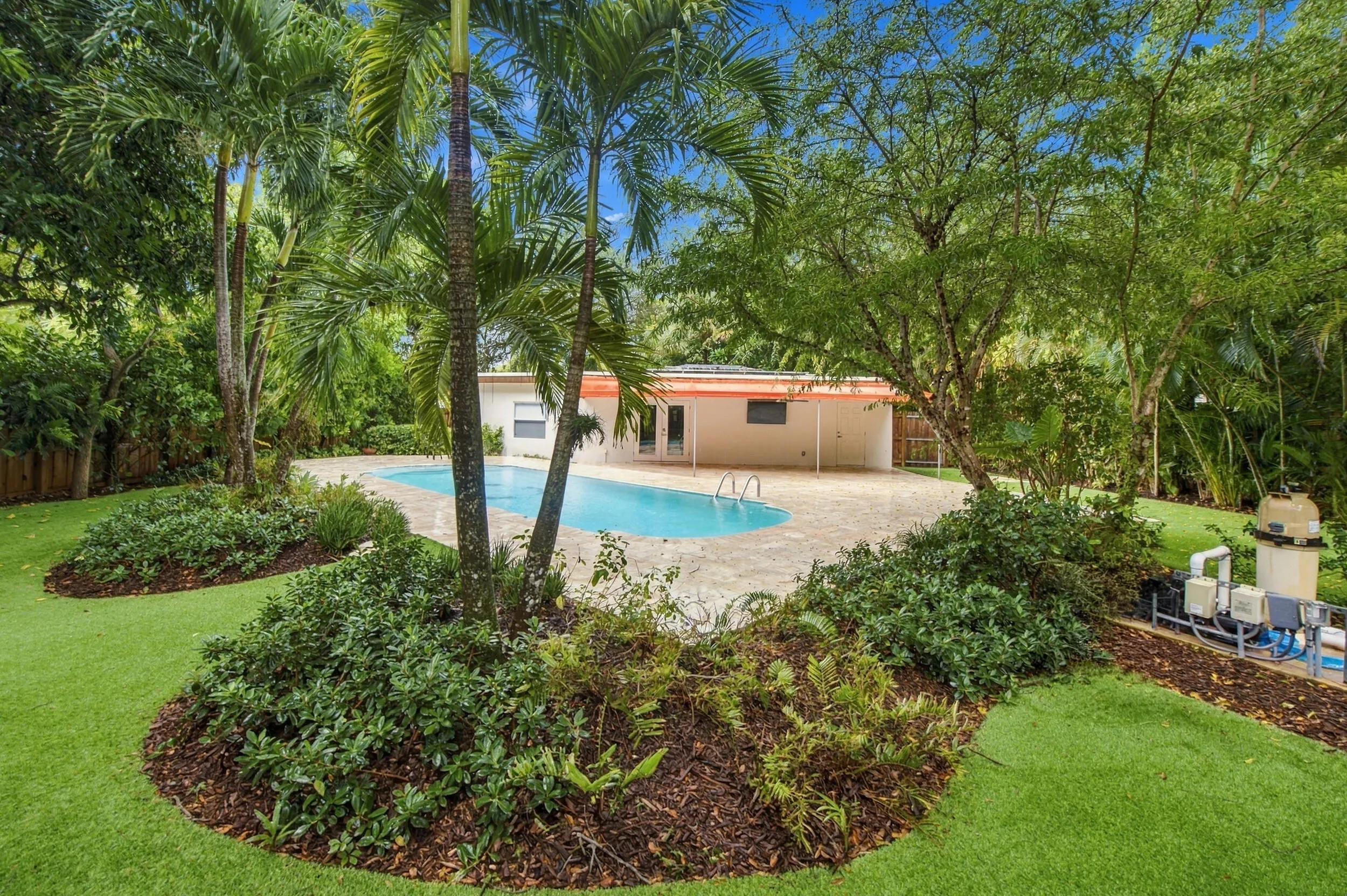 Resort-style backyard featuring a freeform swimming pool, extensive pool decking, and lush tropical landscaping