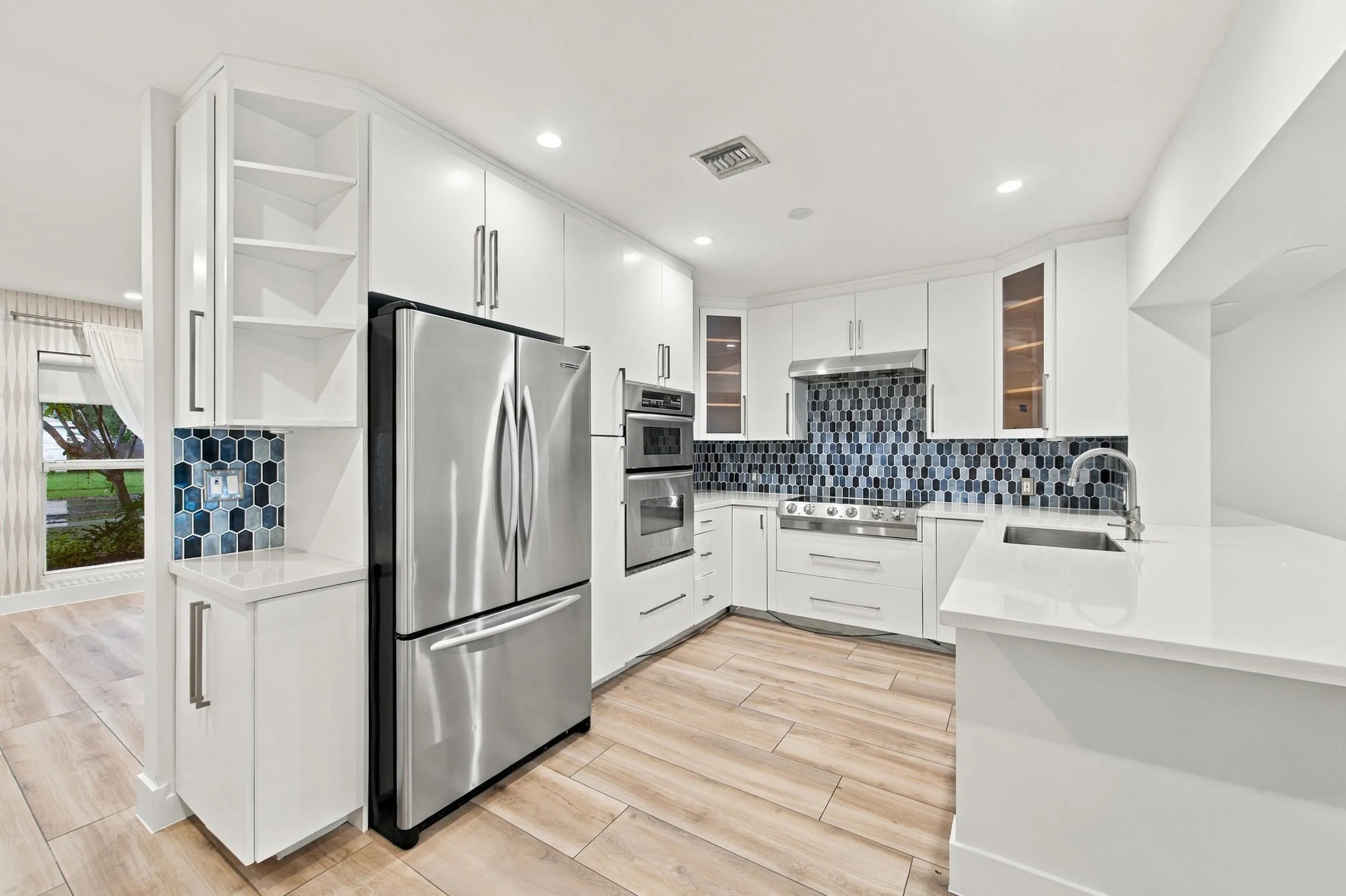 Modern kitchen featuring white cabinetry, stainless steel appliances, a unique blue and black tile backsplash, wood-finish flooring, and white countertops