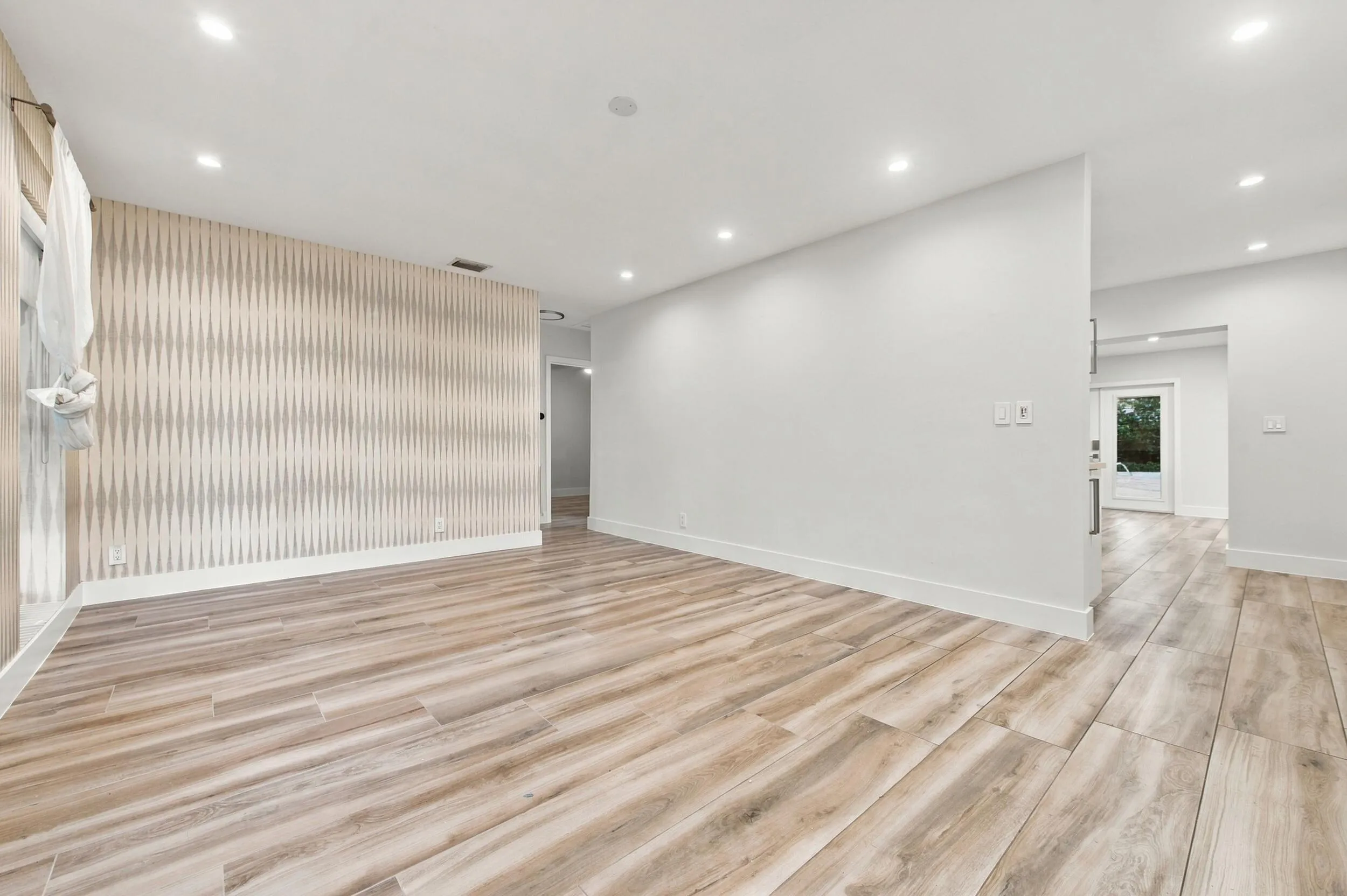 Recessed lighting, wood-finish flooring, accent wall with textured finish, white baseboards, and a glass-paneled door