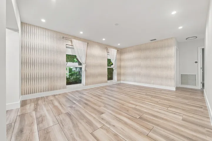 Light wood-finish flooring, recessed ceiling lighting, patterned accent wall, and two windows