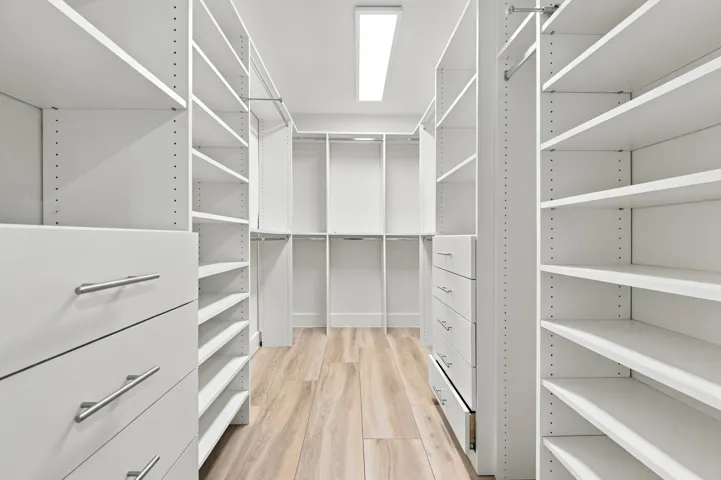 Custom closet system featuring white shelving, integrated drawers with brushed nickel hardware, hanging rods, and wood-finish flooring