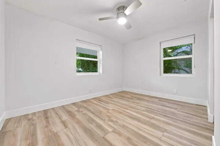 Light-toned wood-finish flooring, white walls, two windows with roller shades, and a ceiling fan with integrated lighting