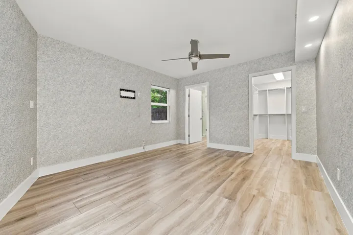 Wood-finish flooring, textured wall finishes, a ceiling fan, recessed lighting, and a walk-in closet with built-in shelving