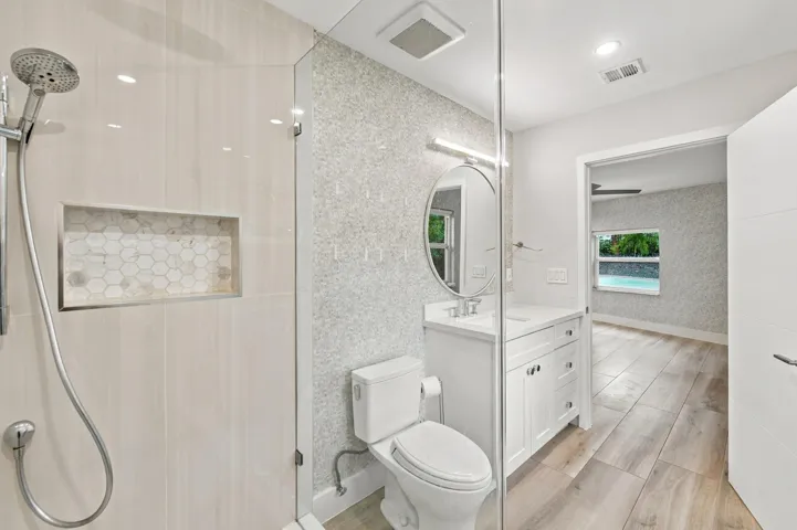 Glass-enclosed shower with a recessed niche, wood-finish flooring, a contemporary vanity with an oval mirror, and recessed lighting