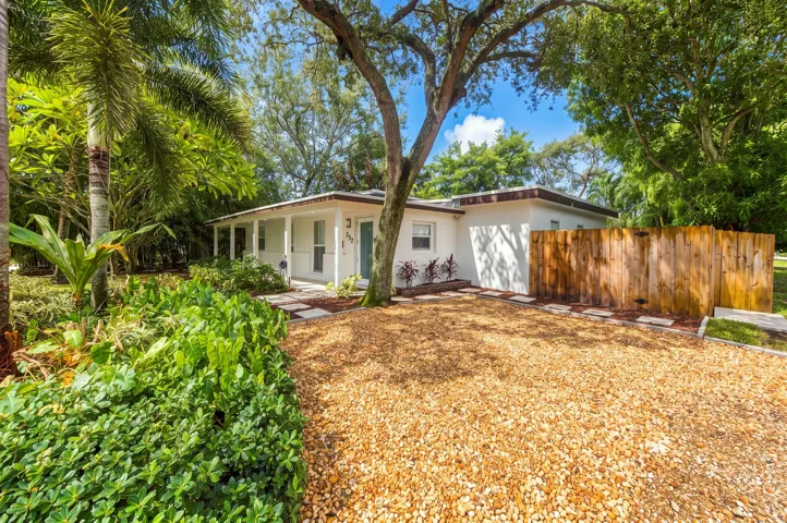 White exterior with covered front porch, gravel driveway, wood privacy fence, and mature landscaping