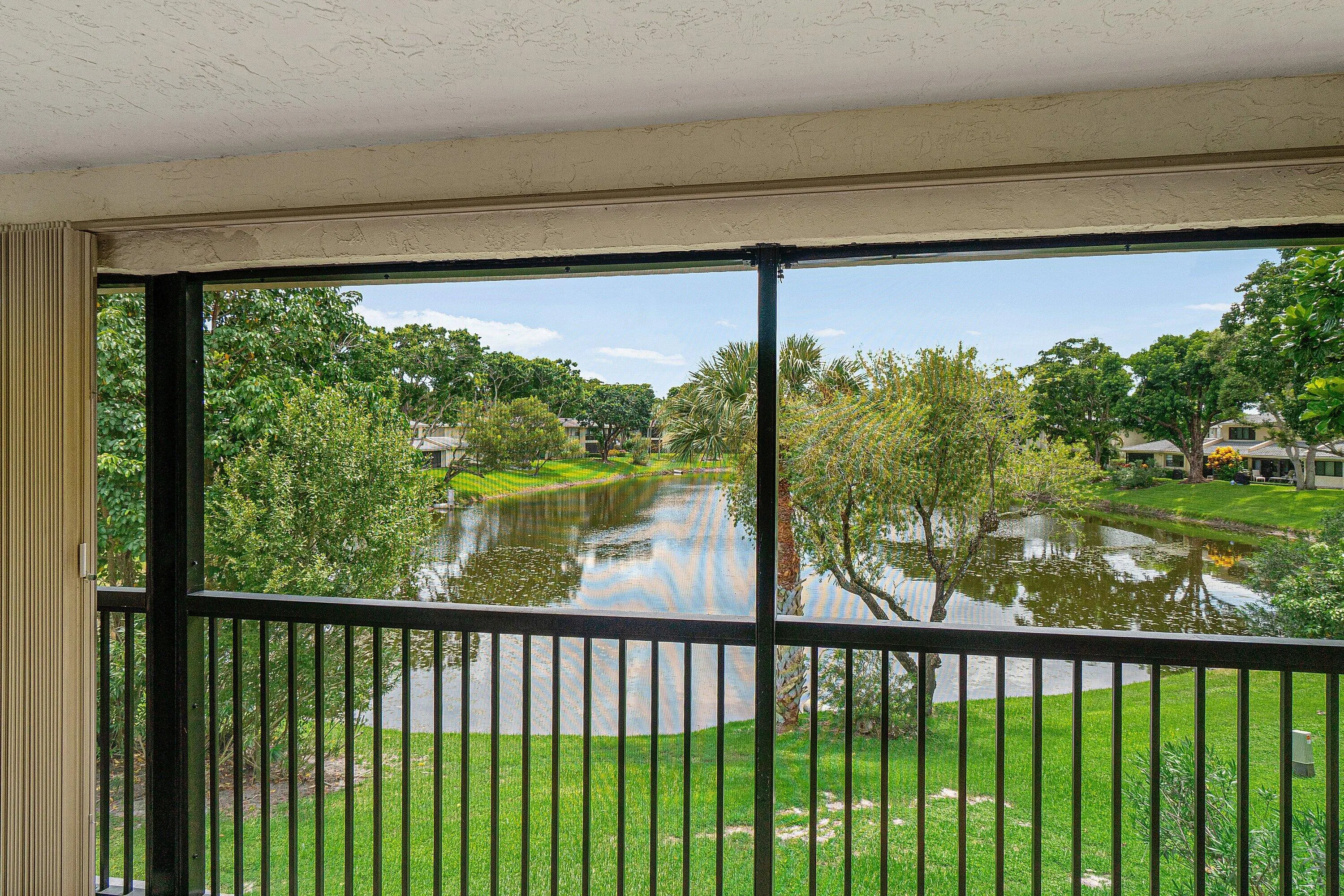 Screened balcony with black metal railings, overlooking a tranquil pond