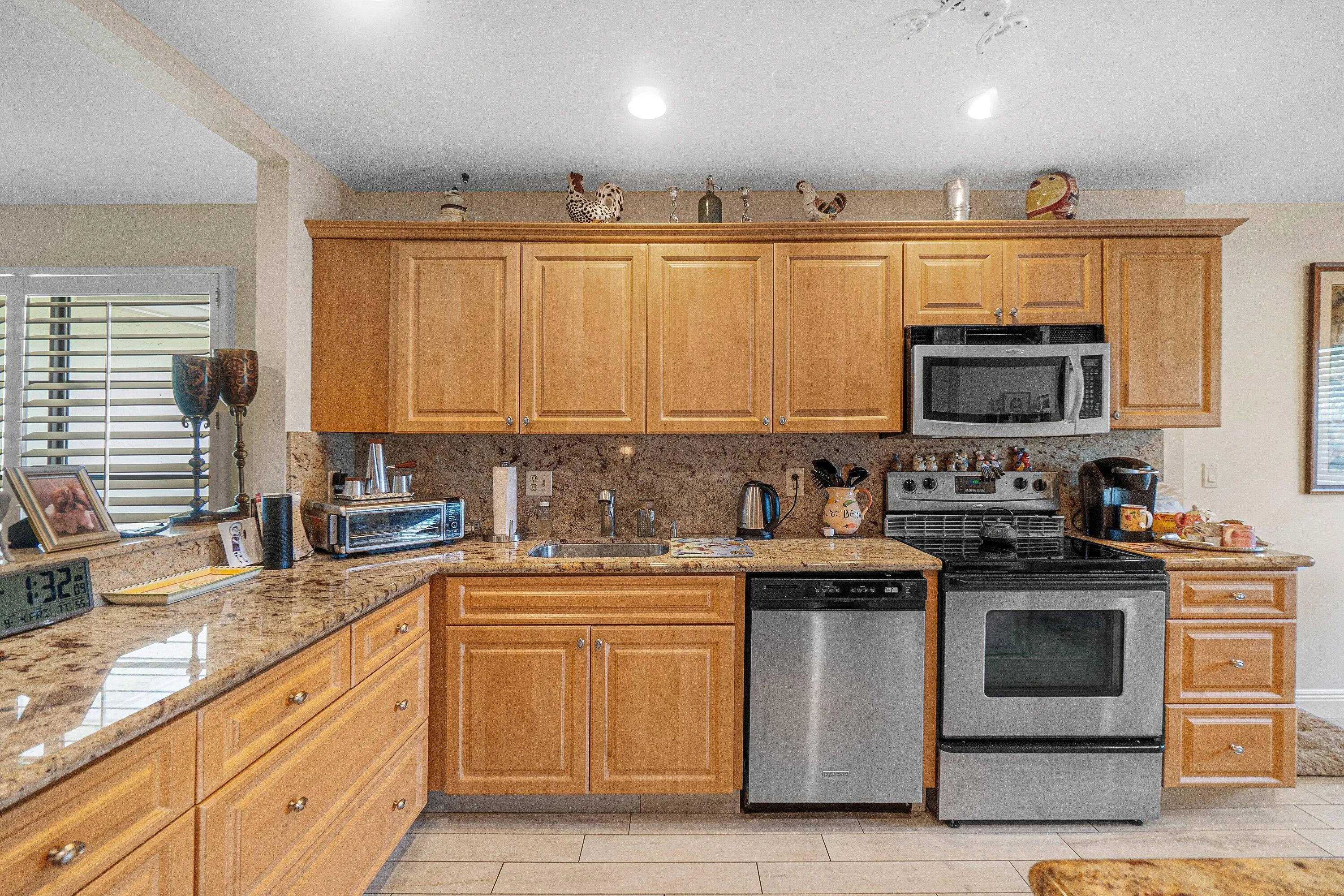 Wood cabinetry with chrome hardware, stone countertops with matching backsplash, stainless steel appliances, and a built-in microwave