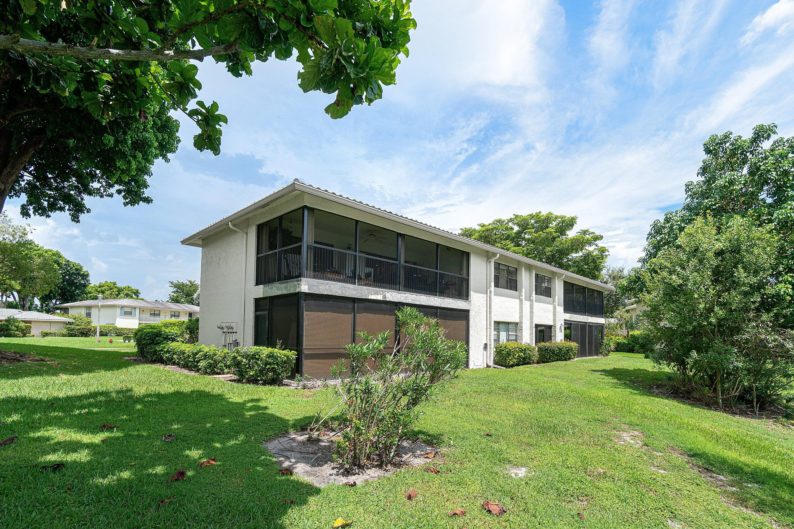 Two-story structure with multiple screened-in balconies and patios, surrounded by mature trees and manicured lawns
