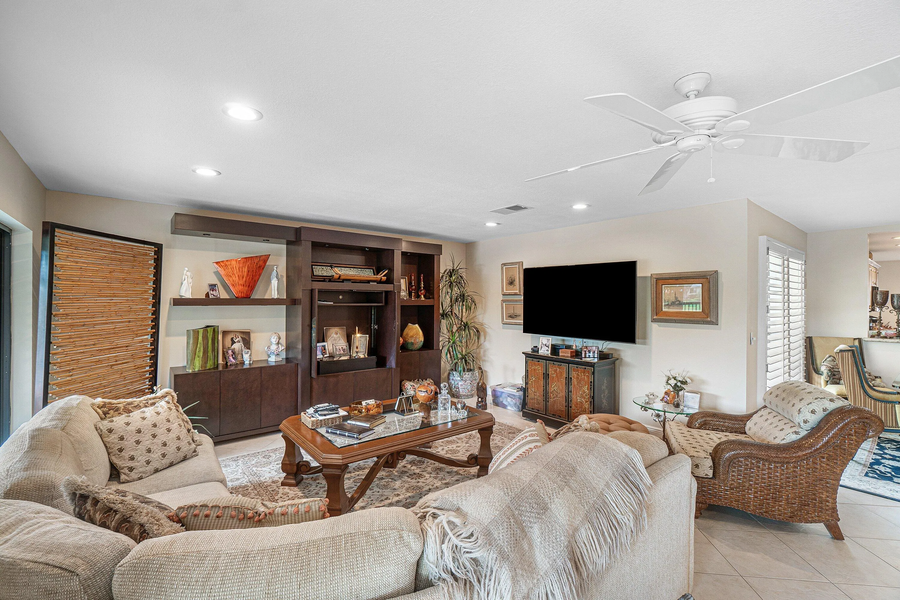 Recessed lighting, ceiling fan, built-in entertainment center with shelving and cabinetry, plantation shutters, and light-toned flooring