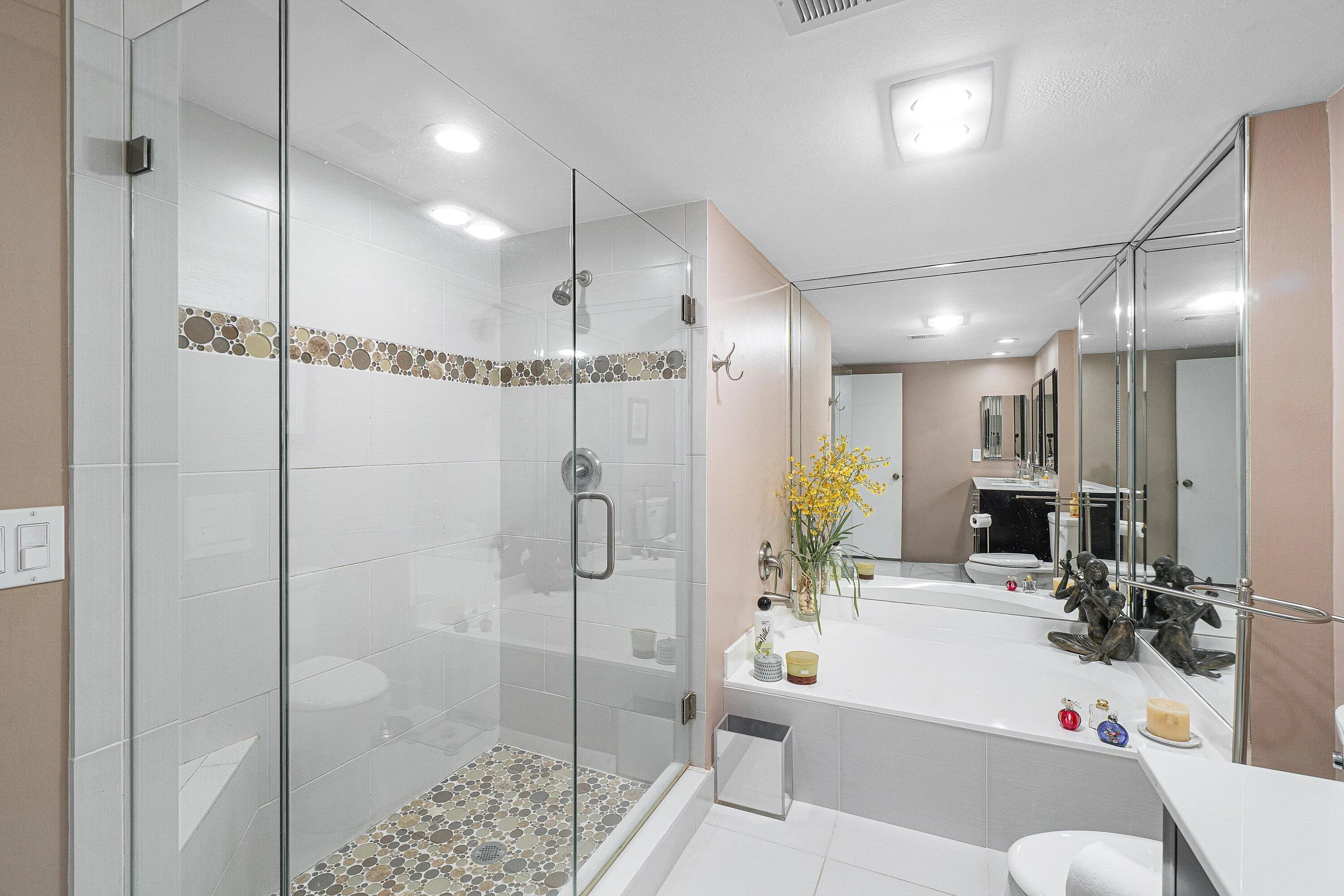 Glass-enclosed shower with a built-in bench, pebble-tile flooring, and a decorative tile band