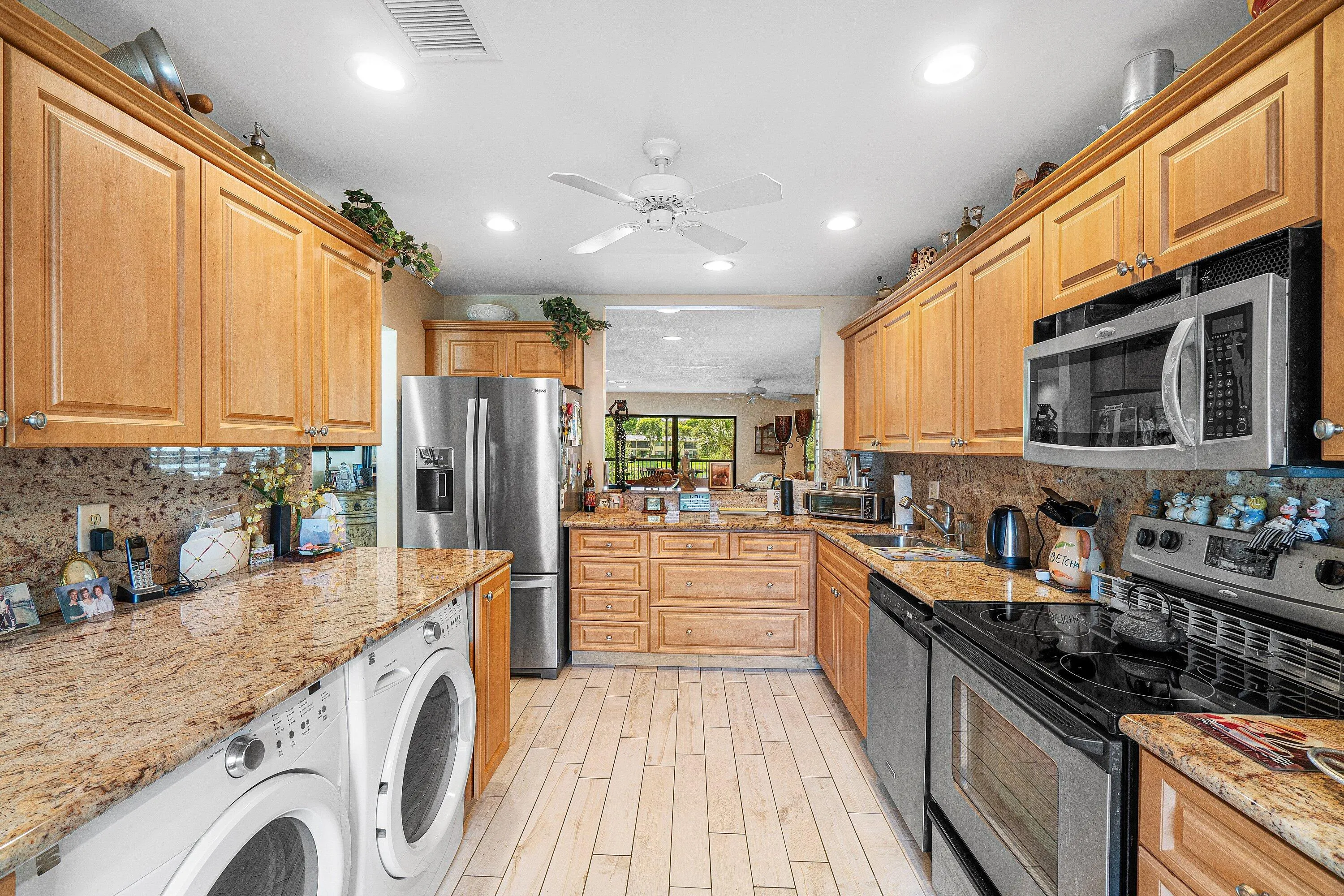 Kitchen featuring abundant wood cabinetry, granite countertops, stainless steel appliances, ceramic tile flooring, and integrated washer and dryer