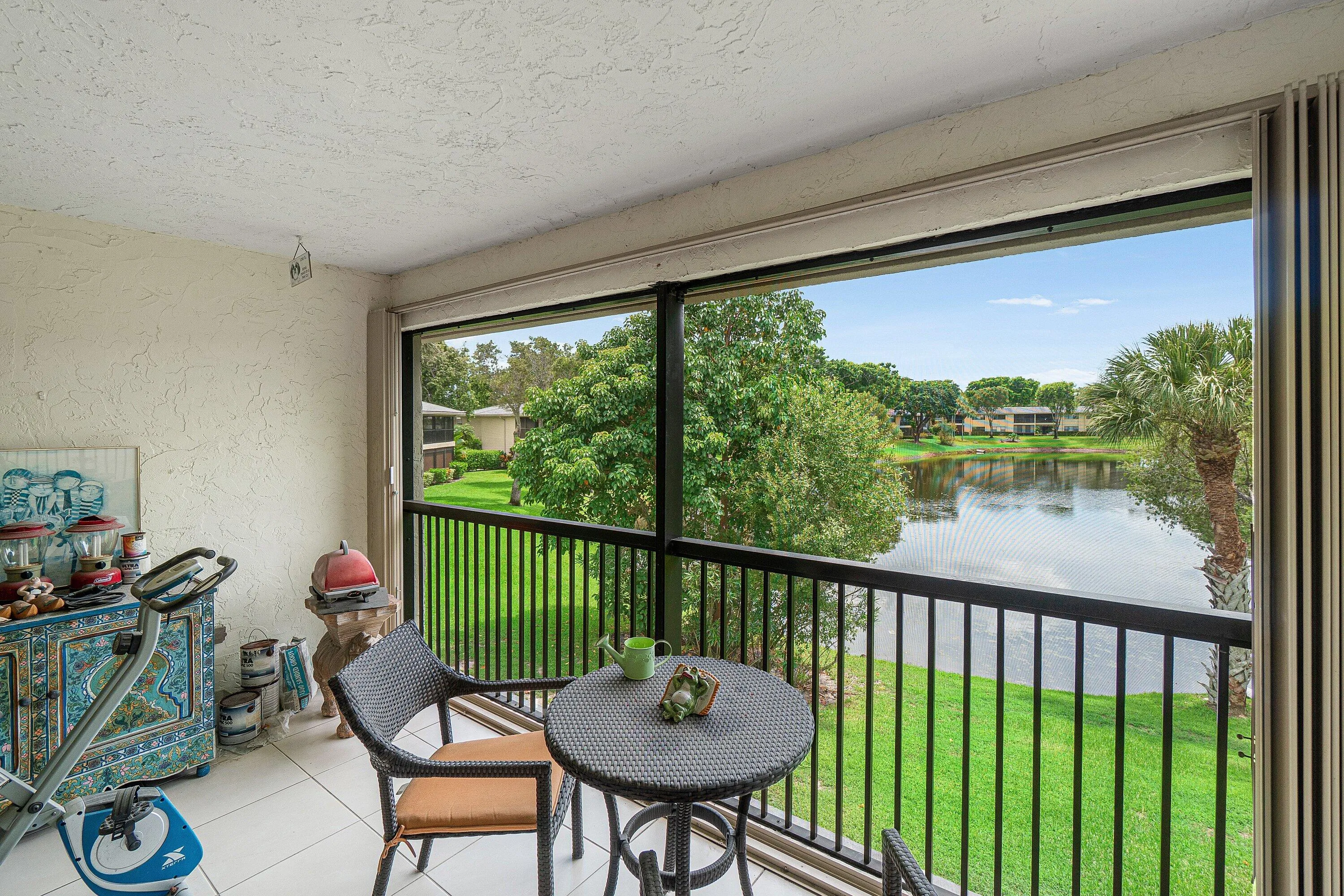 Screened balcony with white tile flooring and a black railing overlooking a lake and mature​​‌​​​​‌​​‌‌​‌‌​​​‌‌​‌​‌​‌​​​‌​​ trees