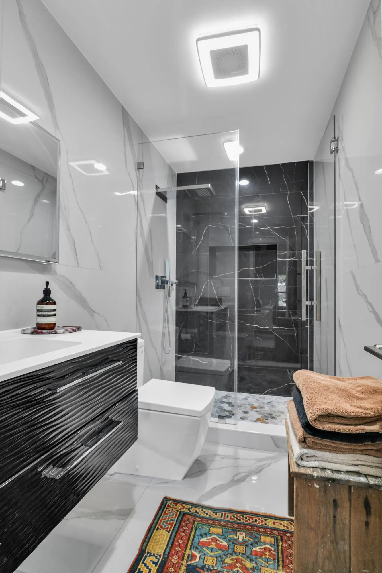 Modern bathroom featuring a glass-enclosed shower with dark-toned tile, wall-mounted vanity with textured drawers, and light-toned tile flooring